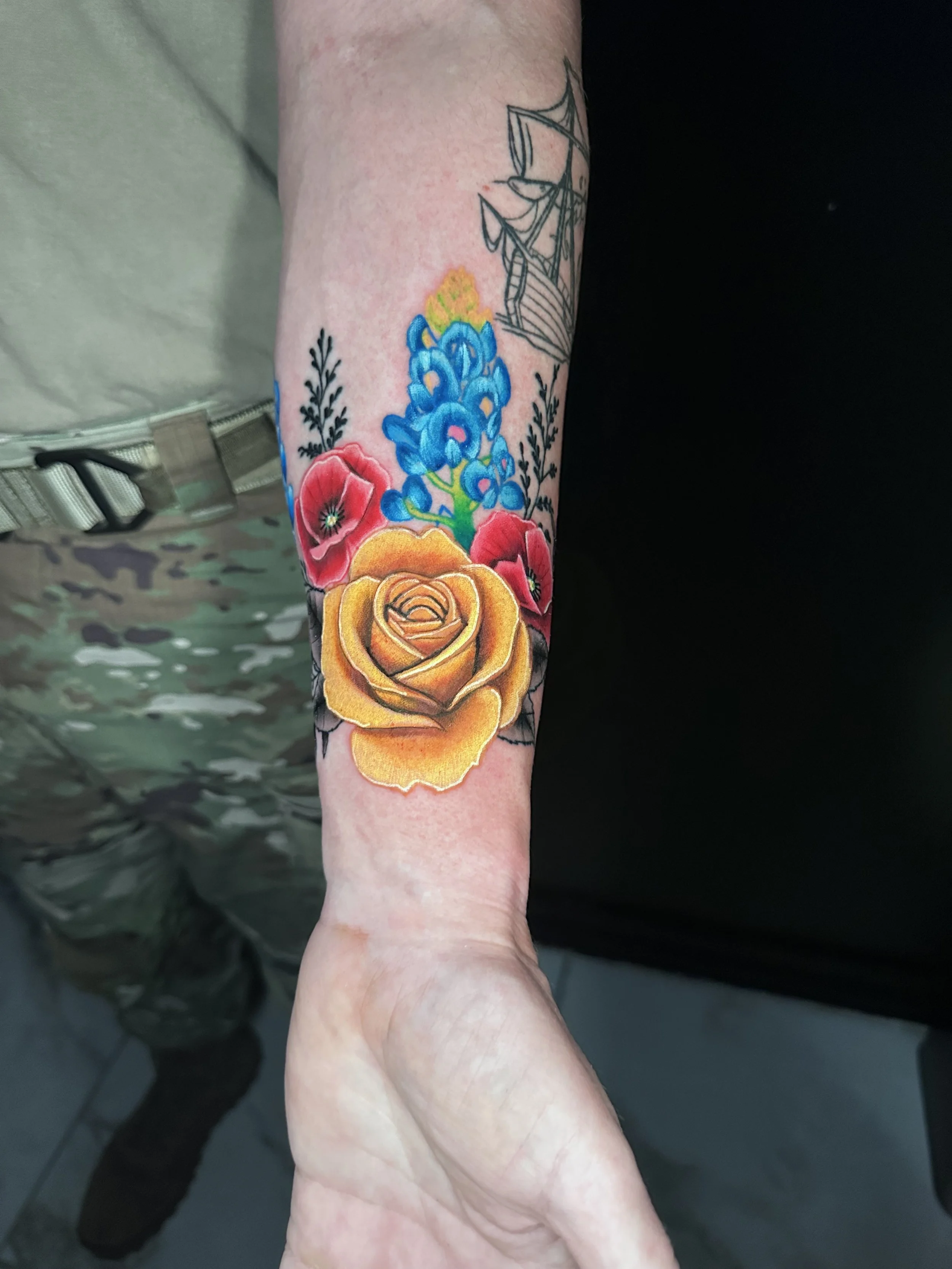 Tattoo on person's arm of a yellow rose, pink poppies, and blue hyacinths with green leaves.