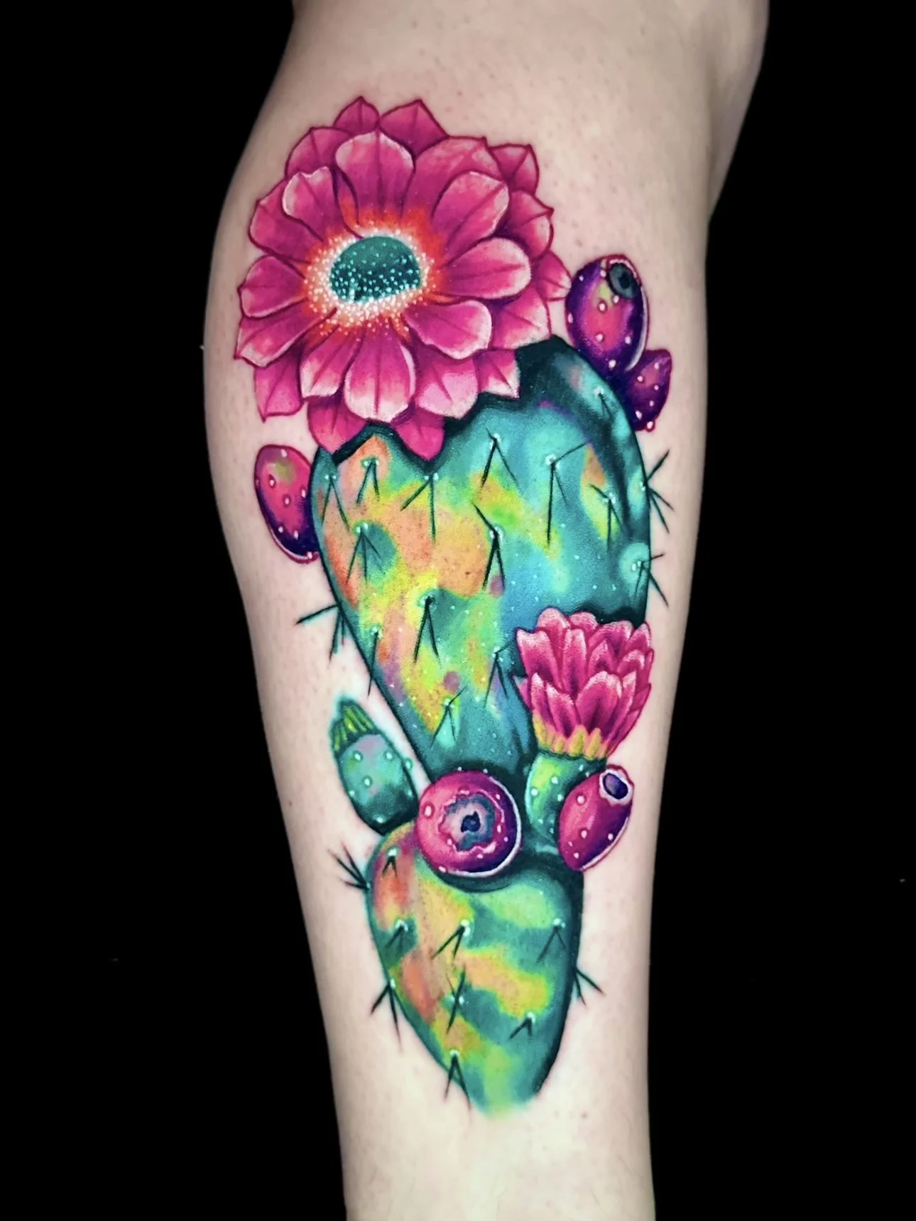 Colorful tattoo of a prickly pear cactus with pink flowers and purple fruit, rendered with a galaxy-like, neon watercolor style.