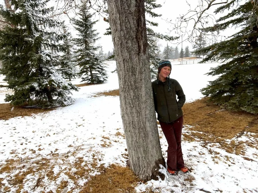 Woman standing by a tree in a snowy forest, symbolizing emotional stillness and feeling stuck in a fight-or-flight state