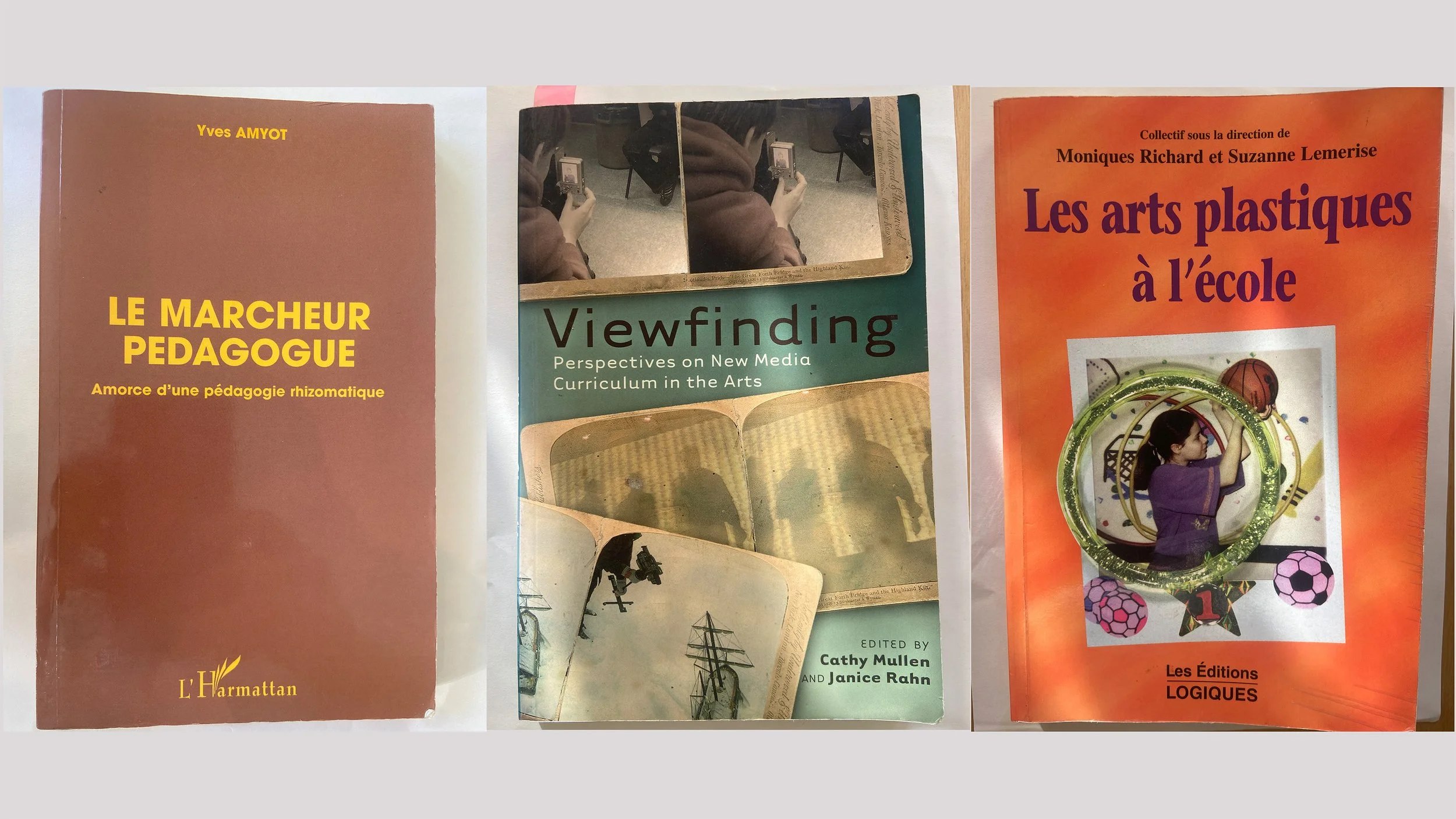 Trois livres empilés. Le premier à gauche est brun avec le titre en jaune 'Le Marcheur Pedagogue'. Le deuxième est vert avec une image de personnes et un titre 'Viewfinding'. Le troisième est orange avec une image d'une jeune fille et un titre 'Les arts plastiques à l'école'.