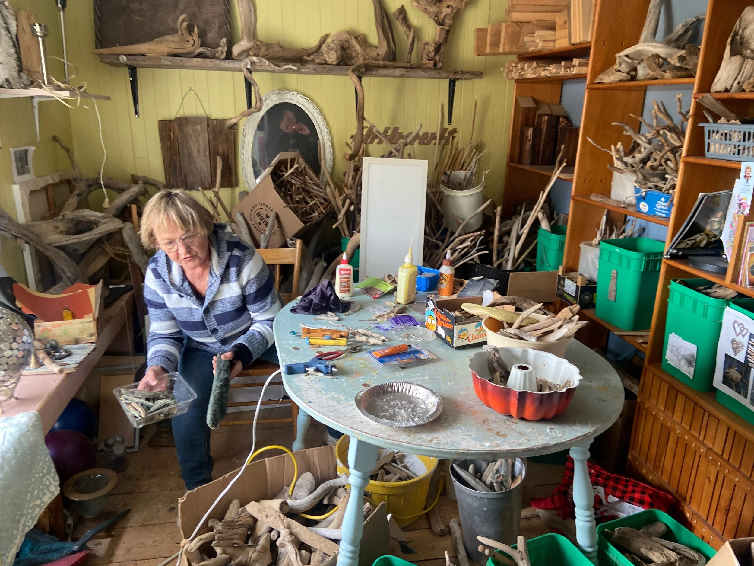 Une femme travaille dans un atelier rempli de bois branchages et outils.