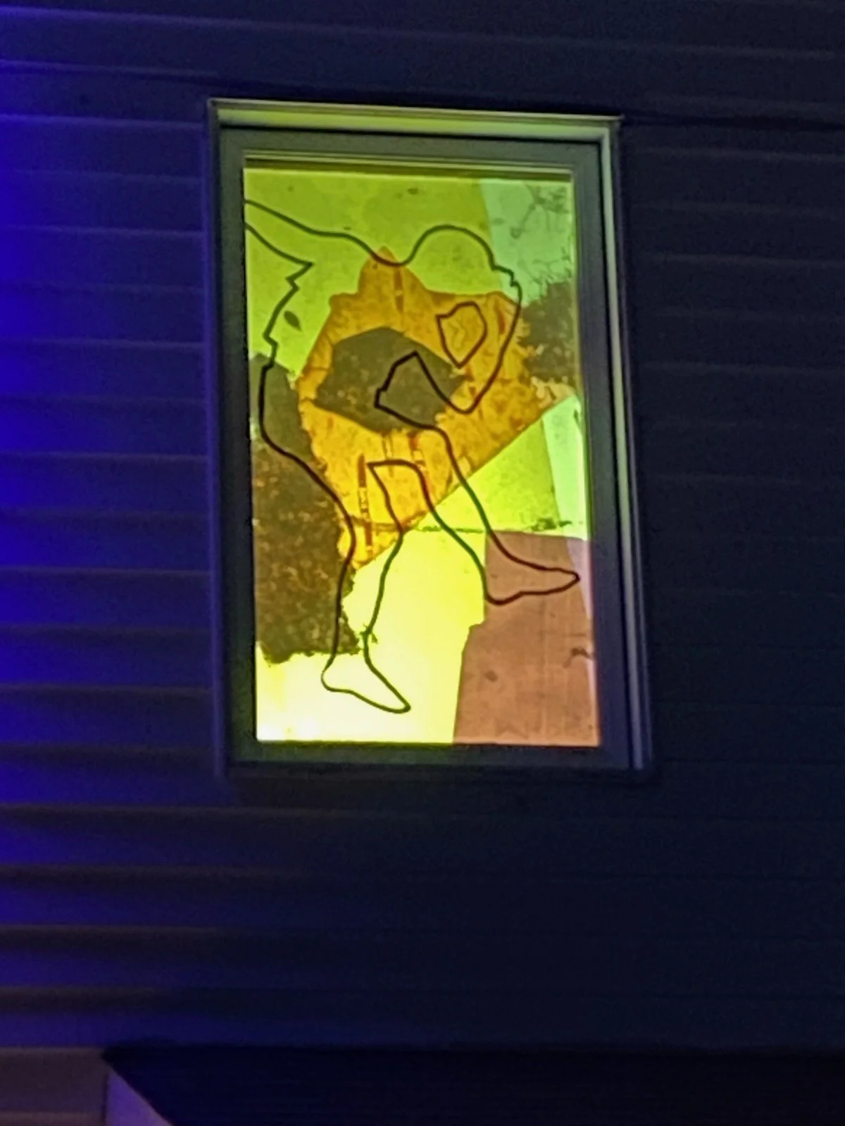 Fenêtre avec une affiche représentant un Pokémon Pikachu stylisé en noir avec un fond coloré en vert, jaune et rouge, situé sur un mur extérieur en bois gris.