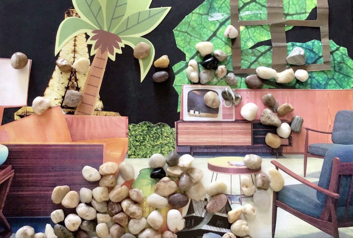 Une scène de décoration intérieure représentant un salon avec un mur en papier peint à motif feuille, une fausse cheminée, des meubles en bois, des pierres de différentes couleurs disposées pour donner l'impression d'une forêt ou d'une nature sauvage