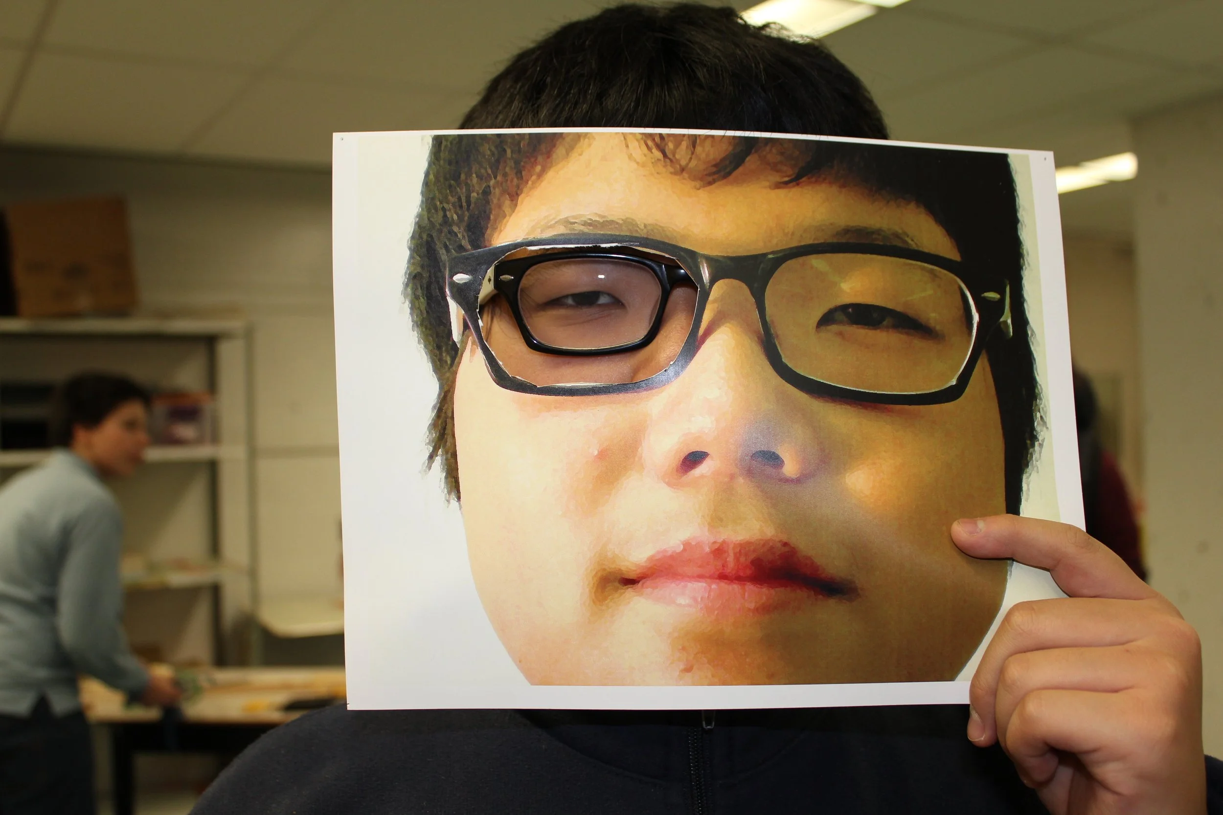 Personne tenant un poster représentant un visage d'enfant avec des lunettes, faisant semblant que le poster est leur visage.