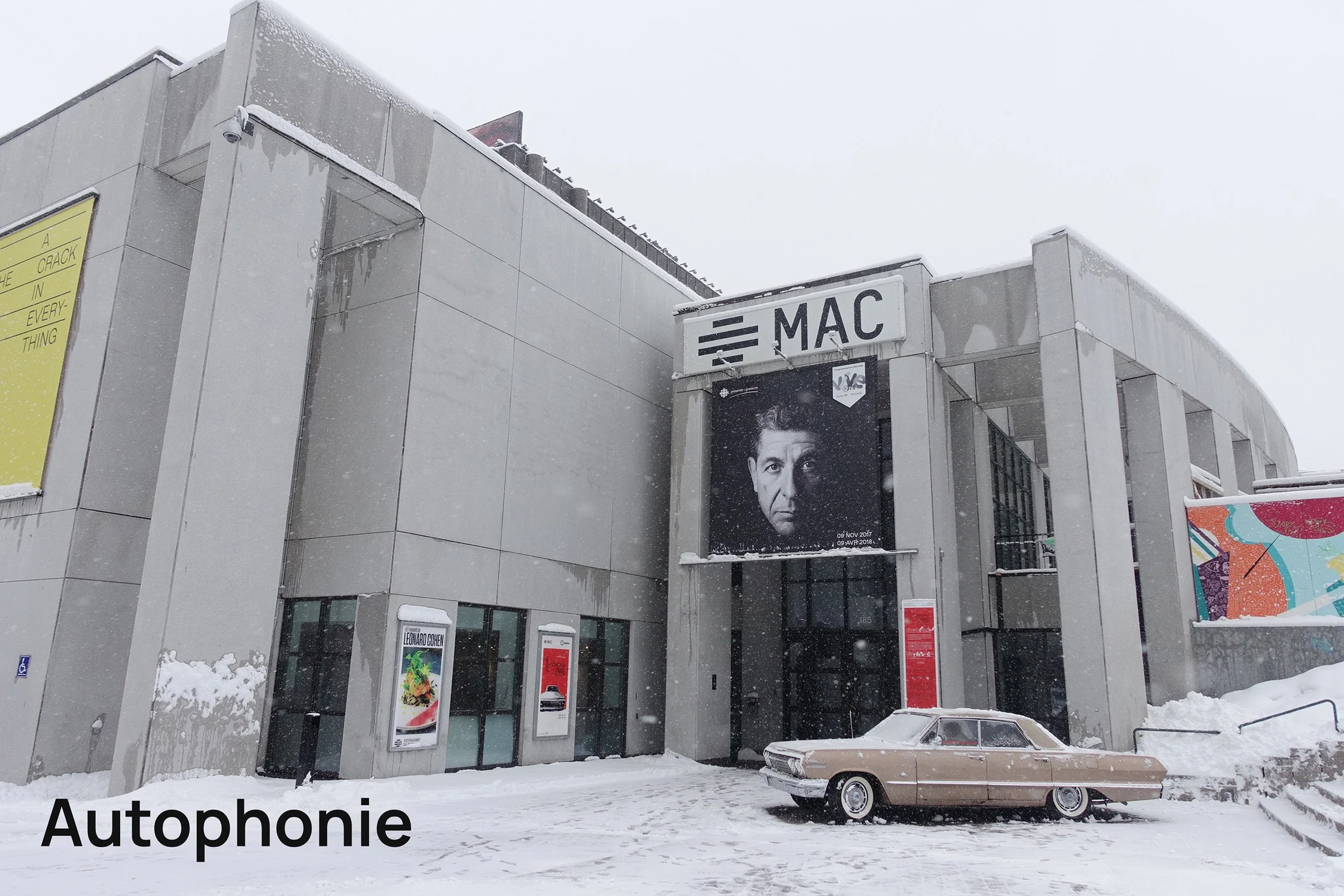 Bâtiment moderne avec panneau d'affichage noir et blanc d'un homme, neige au sol, voiture ancienne beige garée devant, hiver, Mac, affiches publicitaires.