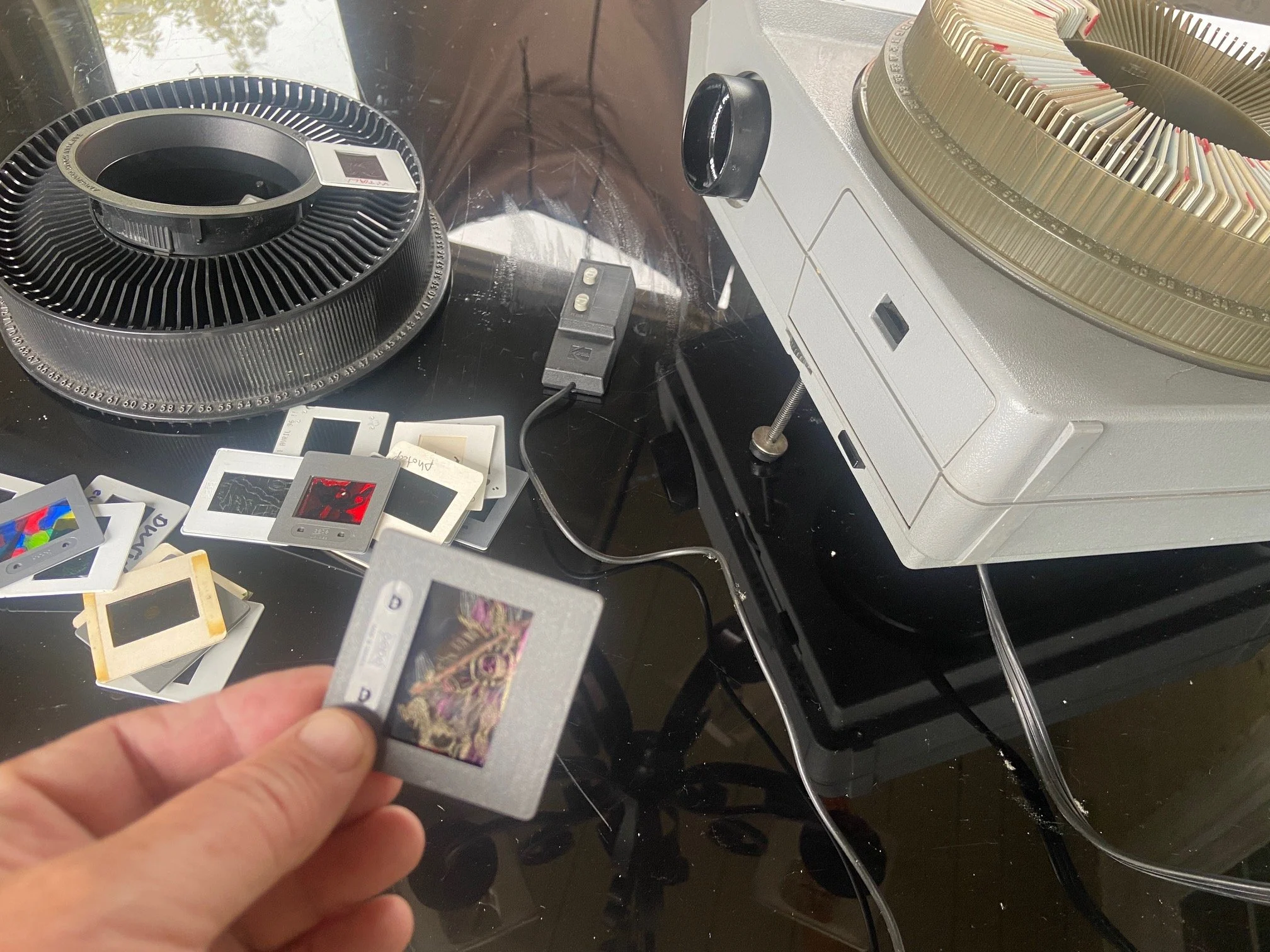 Une main tient une carte de jeu Pokémon à côté d'une arcade Pokémon, avec d'autres cartes et un tourne-disque vintage sur une table noire.