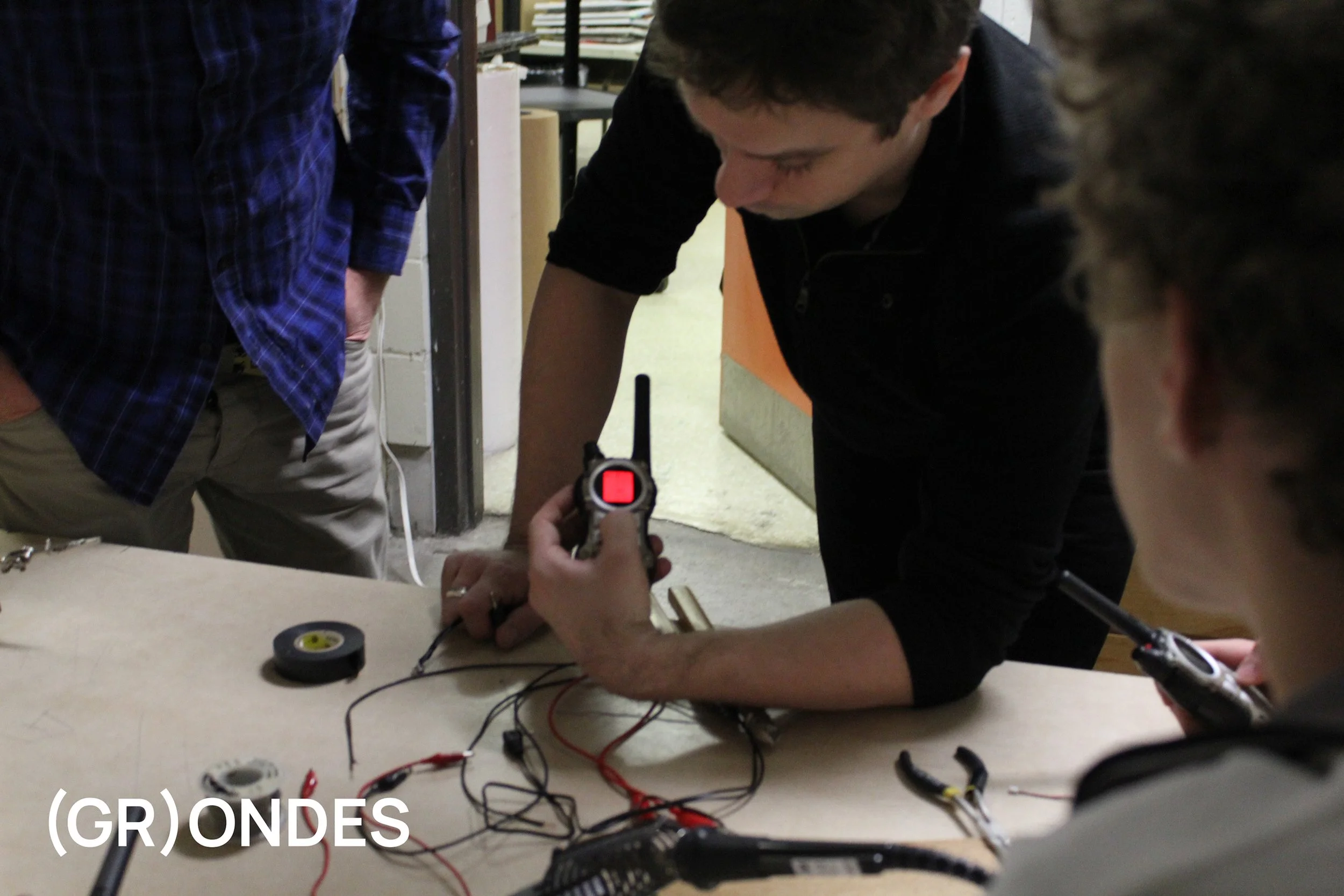 Groupe de personnes travaillant sur un projet électronique avec des outils et des fils sur une table.