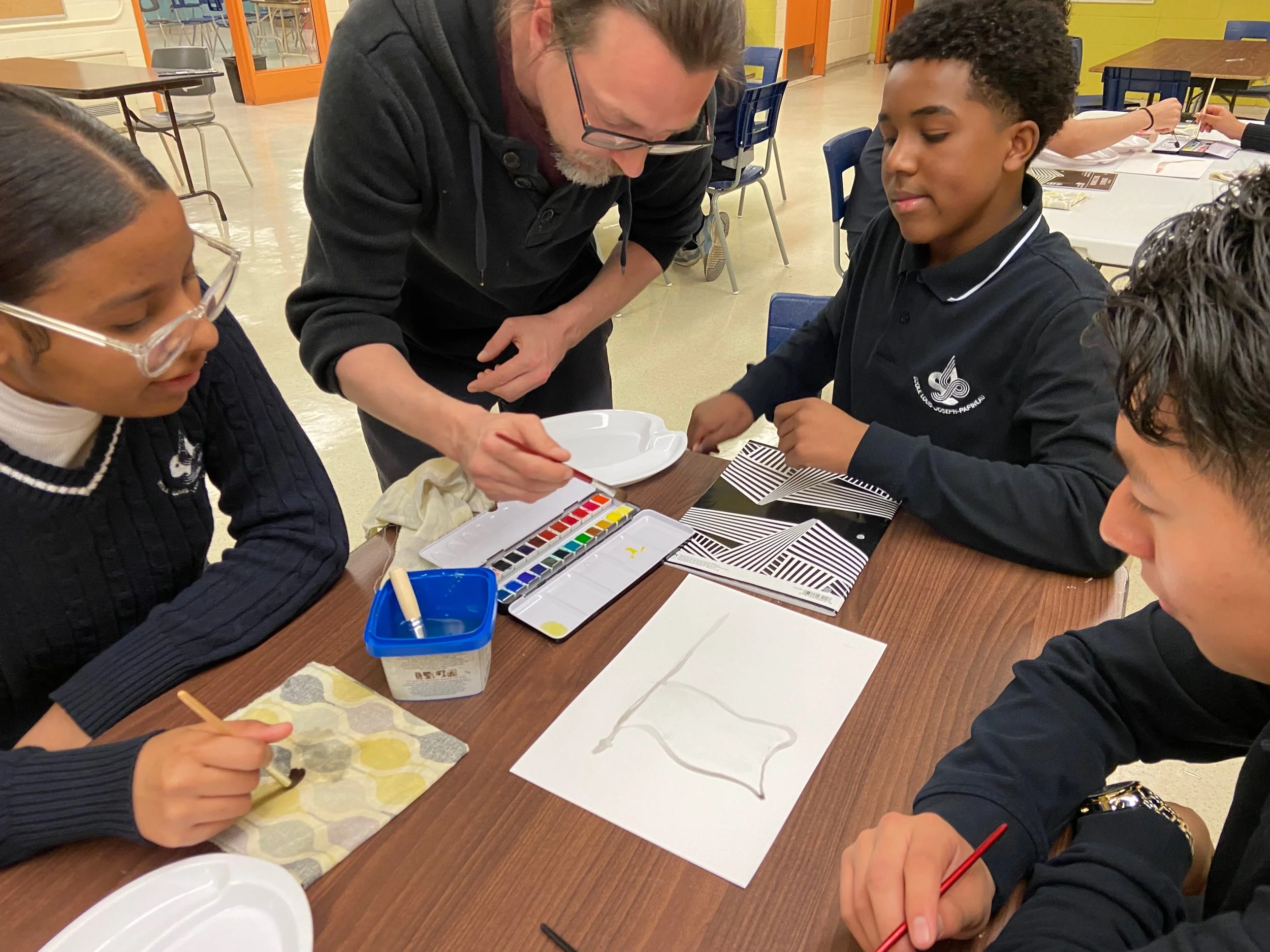 Un groupe d'enfants et un adulte participent à une activité artistique avec de la peinture et des pinceaux sur une table en intérieur.