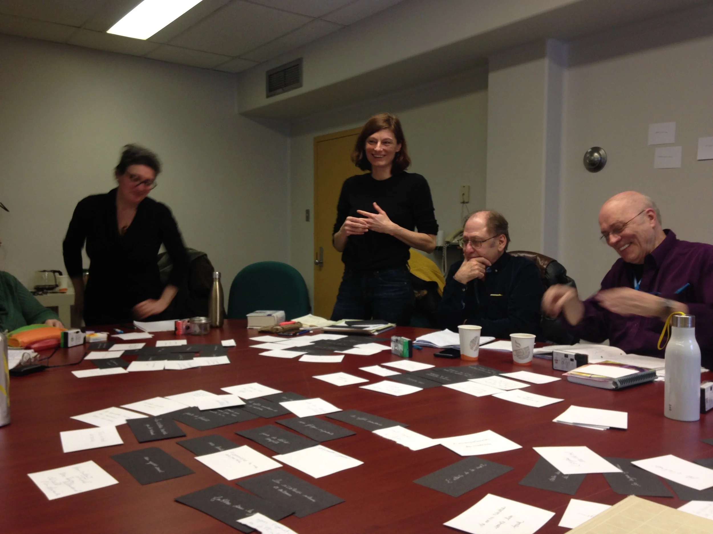 Groupe de personnes autour d'une table lors d'une réunion ou d'une activité de groupe, avec des cartes, des notes et des boissons sur la table.
