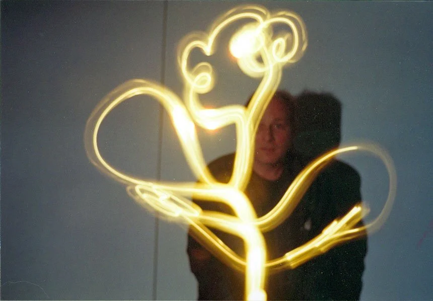 Une personne pose devant une lumière qui trace un dessin de fleur lumineux dans l'air.