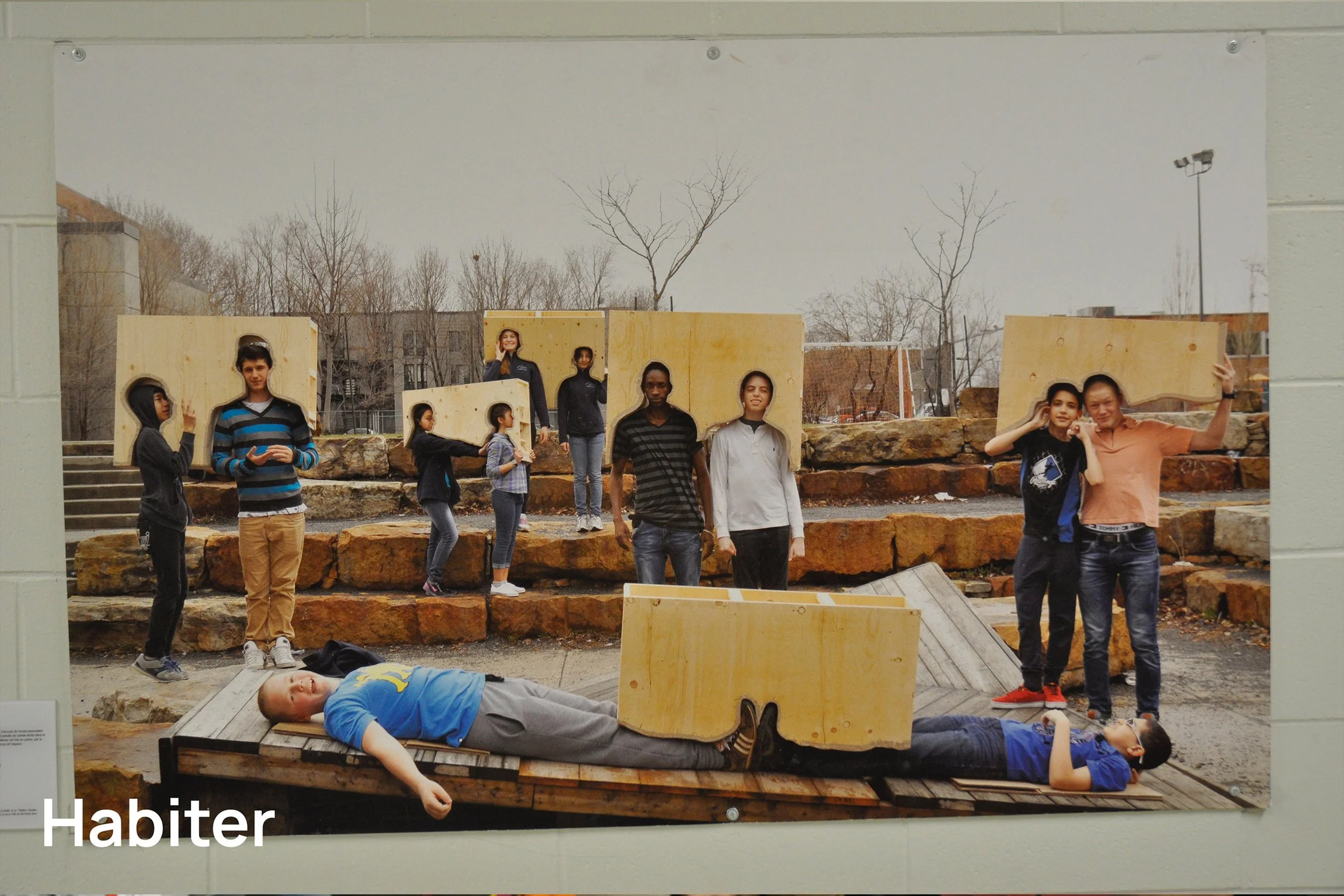 Une photo d'un groupe de jeunes en extérieur, avec des personnes posant ou interagissant, dans un environnement urbain avec des rochers et un décor de ville en arrière-plan.