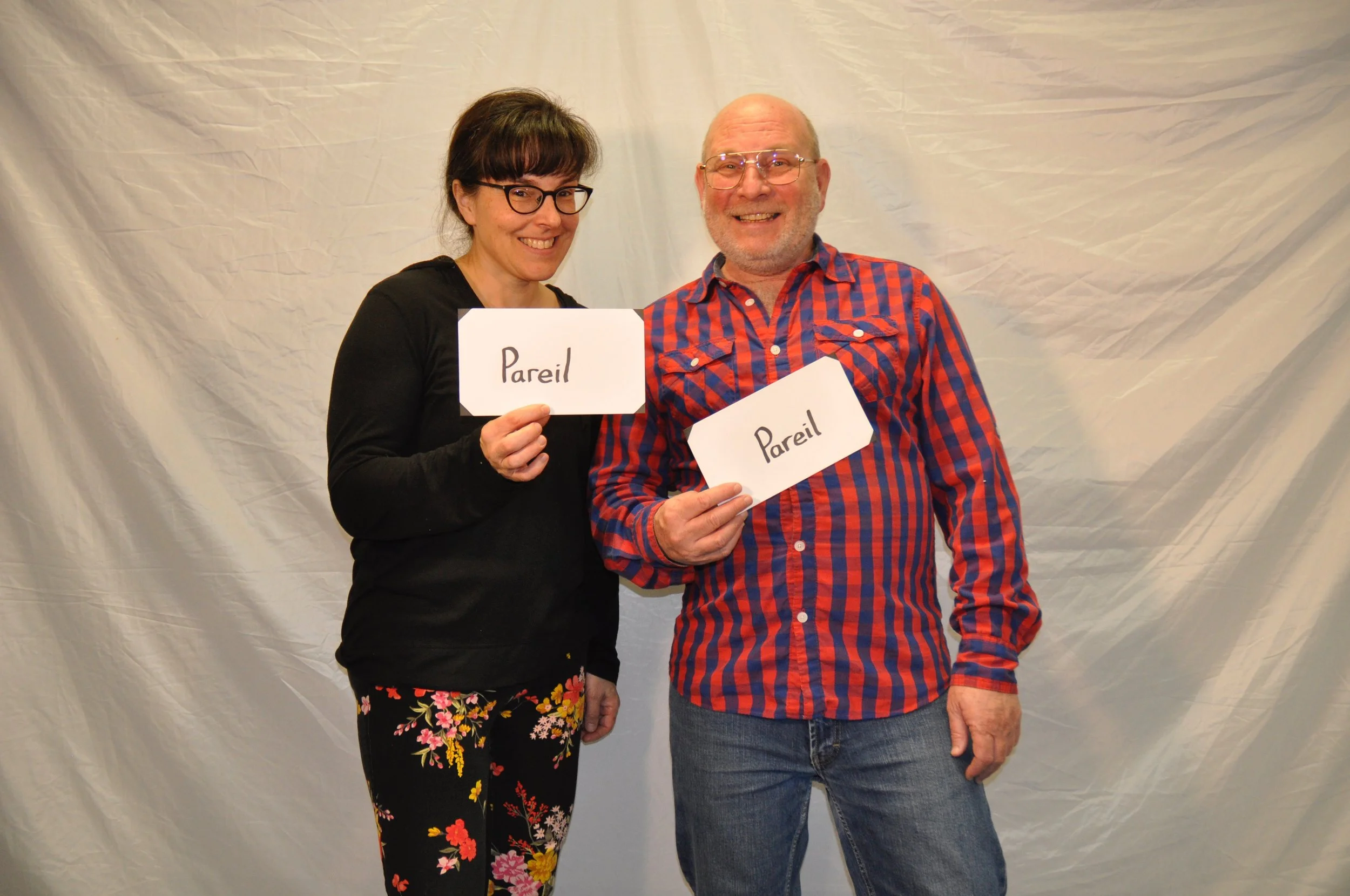 Deux personnes, un homme et une femme, tenant des panneaux avec le mot 'Pareil', posant devant un fond blanc.