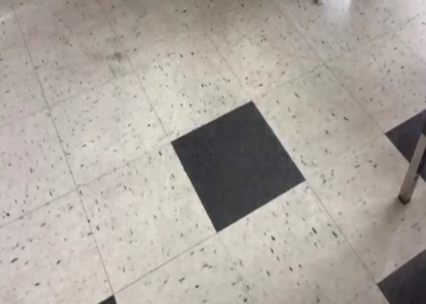 Sol en terrazzo avec un carreau noir au centre, vue partielle avec une structure métallique en bas à droite.