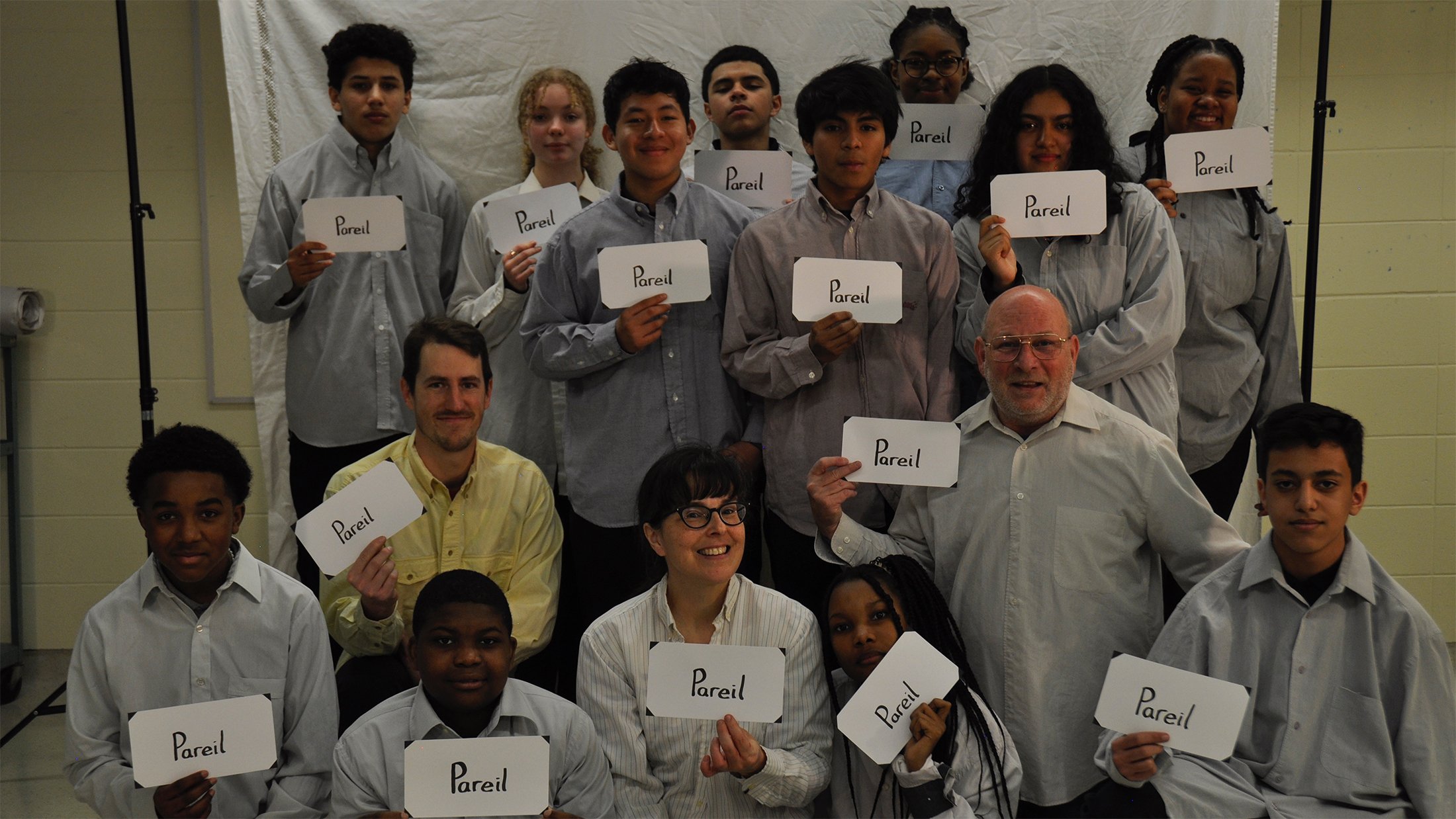 Groupe de personnes en atelier, montrant des pancartes avec le mot 'Pareil' écrit dessus, dans une pièce avec un fond blanc.