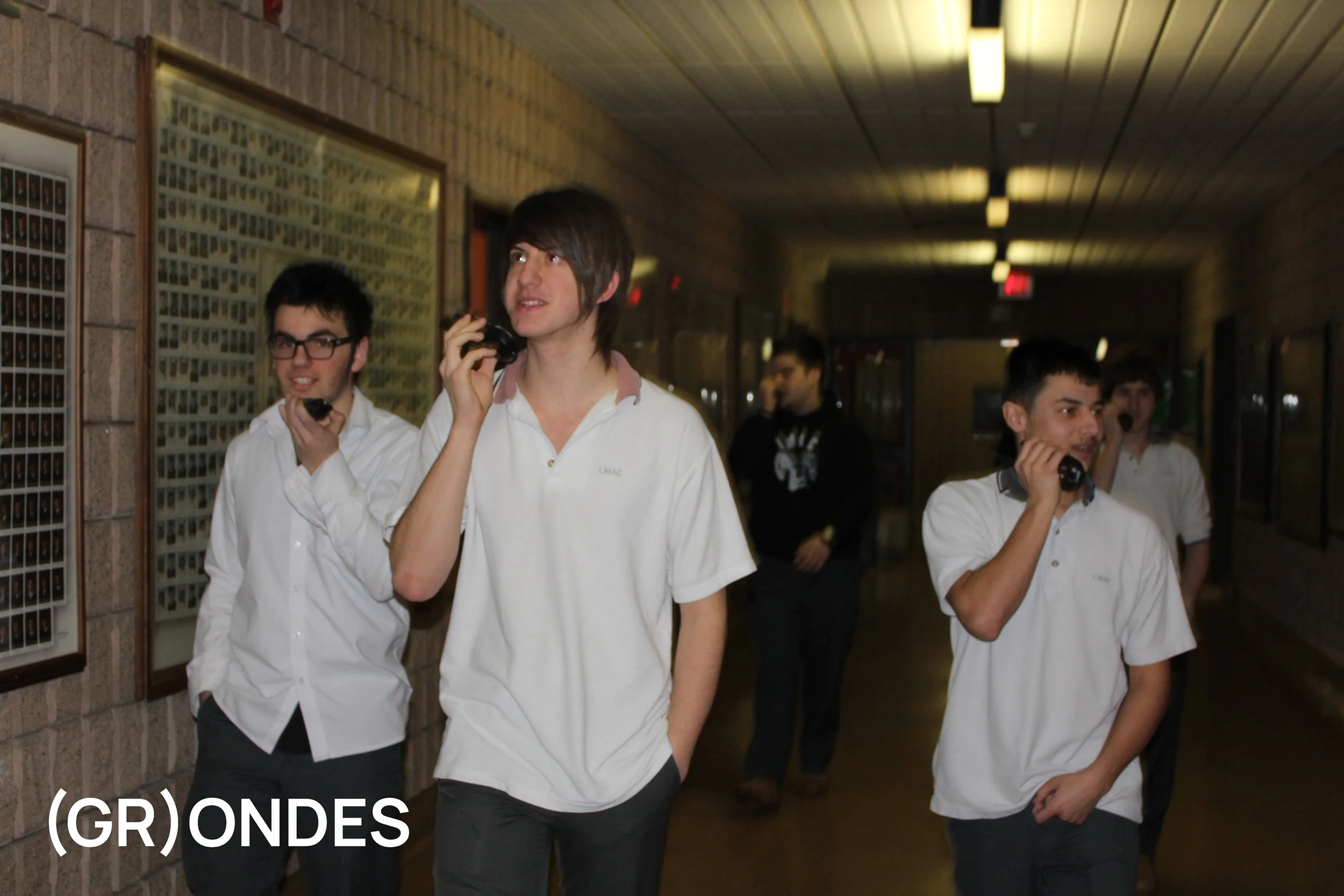 Groupe de jeunes hommes en uniforme blanc, parlant au téléphone dans un couloir d'école
