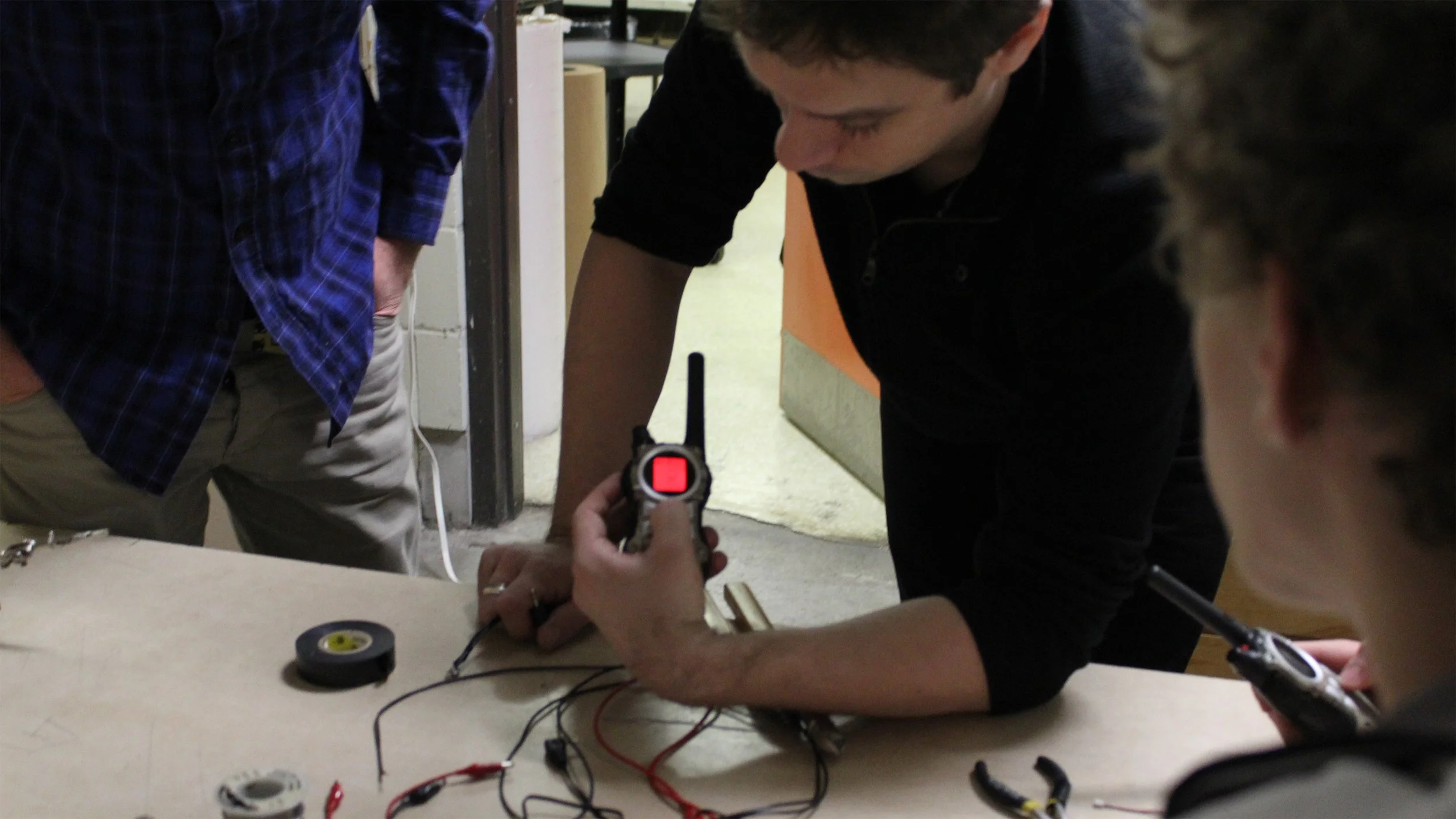 Trois personnes à une table en train de tester un appareil électronique avec des fils et un pistolet à impulsions, dans une pièce