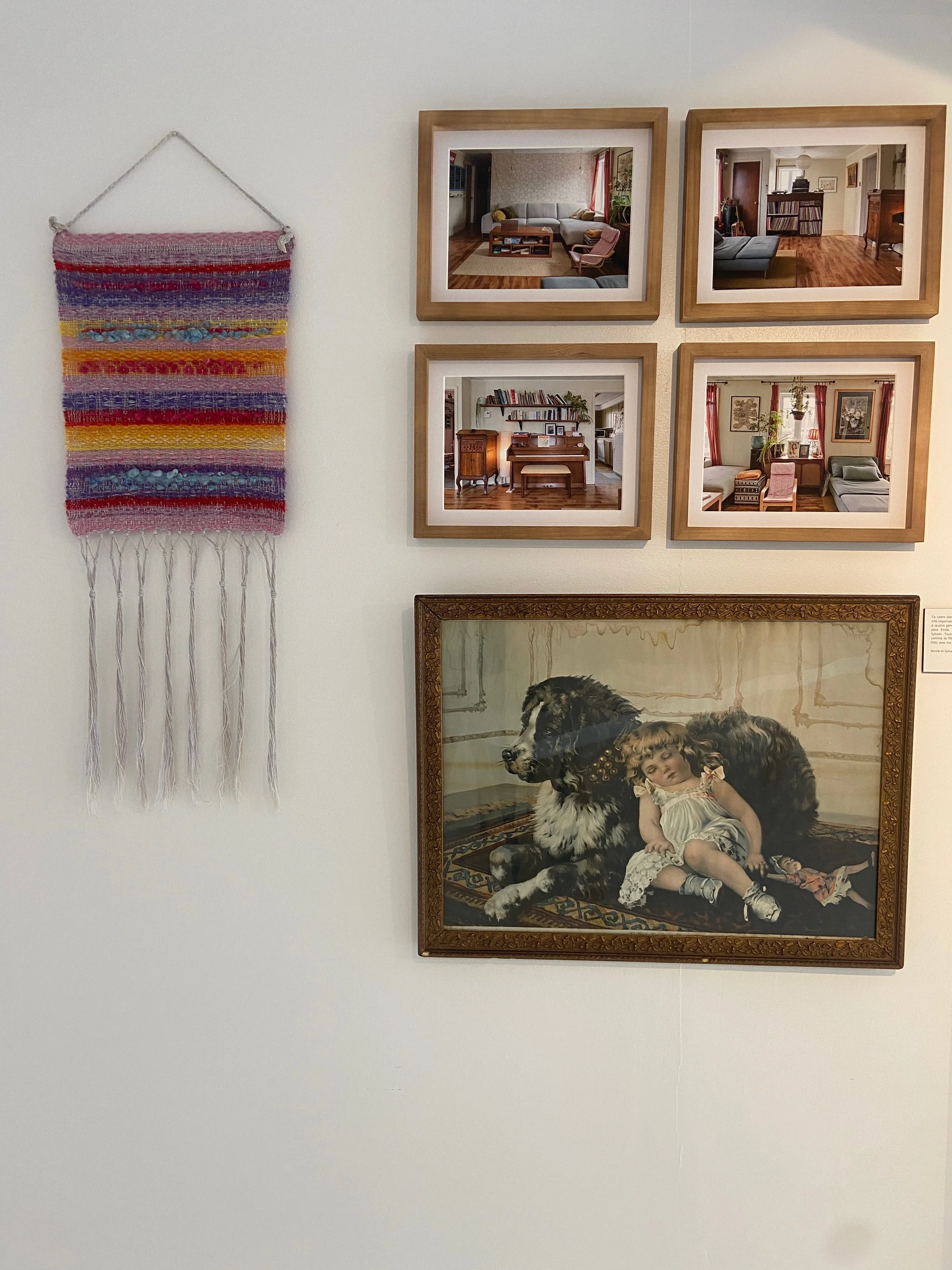 Mur avec 4 cadres de photos de l'intérieur d'une maison, un tapis mural coloré à franges sur le côté gauche, et un tableau d'une fille et un chien