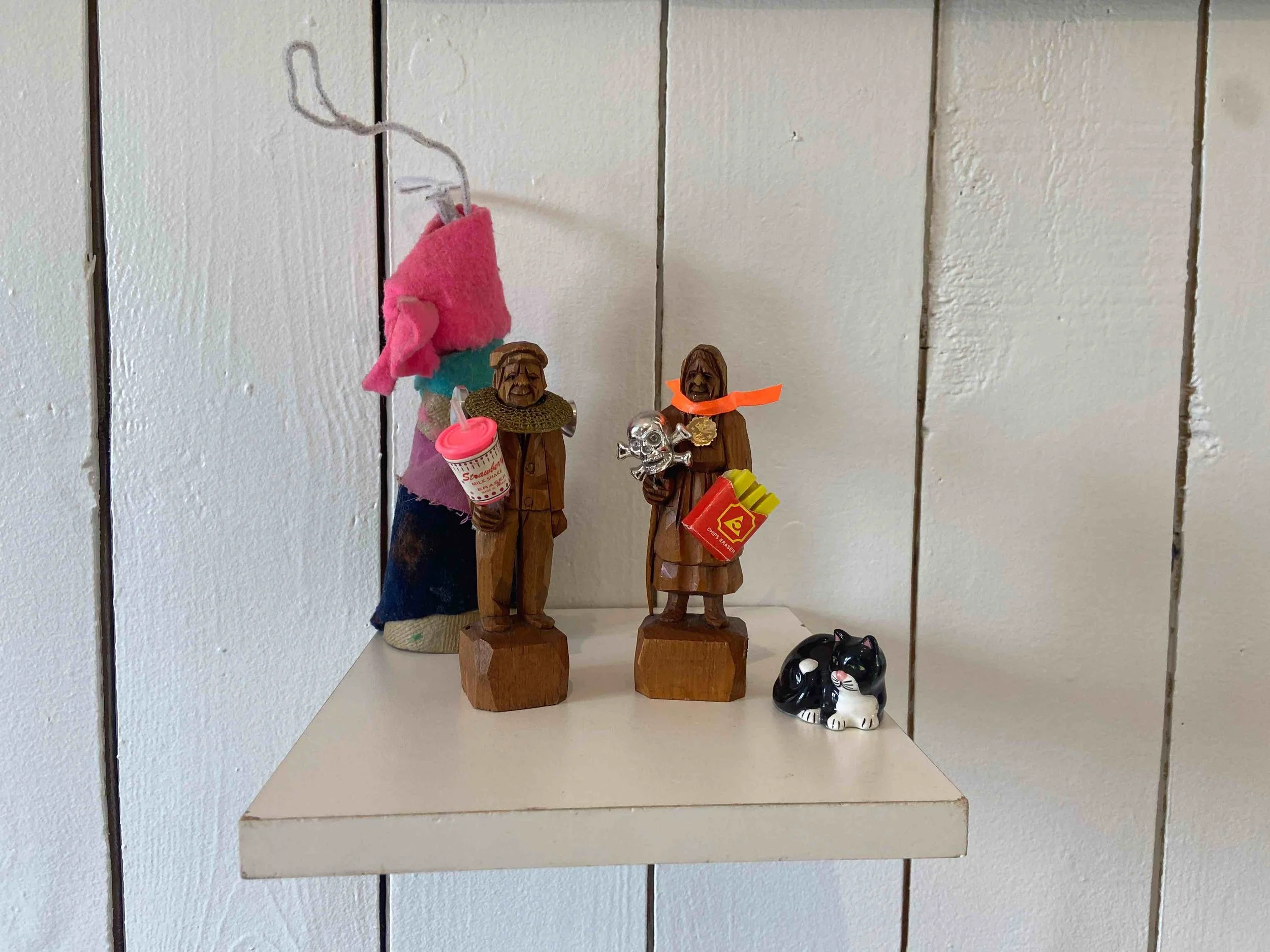 Petites figurines en bois représentant des personnes anciennes avec des accessoires tristes ou amusants, une petite figurine de chat noir et blanc.