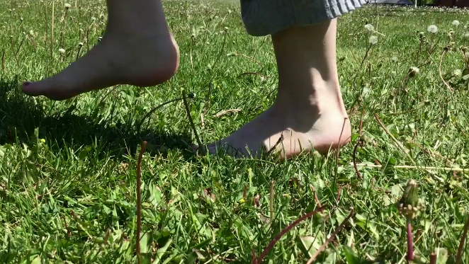 Deux personnes marchent pieds nus sur l'herbe verte et fleurie d'un champ.
