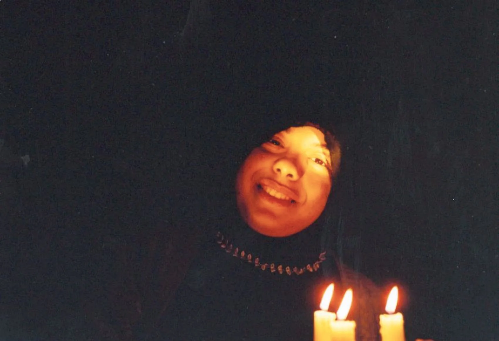 Une personne souriante avec un visage illuminé par la lumière de bougies dans l'obscurité.