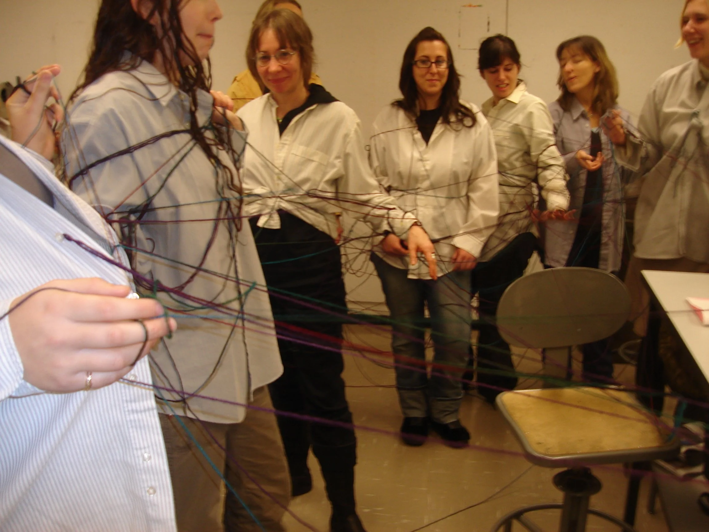 Groupe de femmes portant des blouses claires, participent à une activité de groupe avec de la laine de différentes couleurs, dans une salle intérieure.