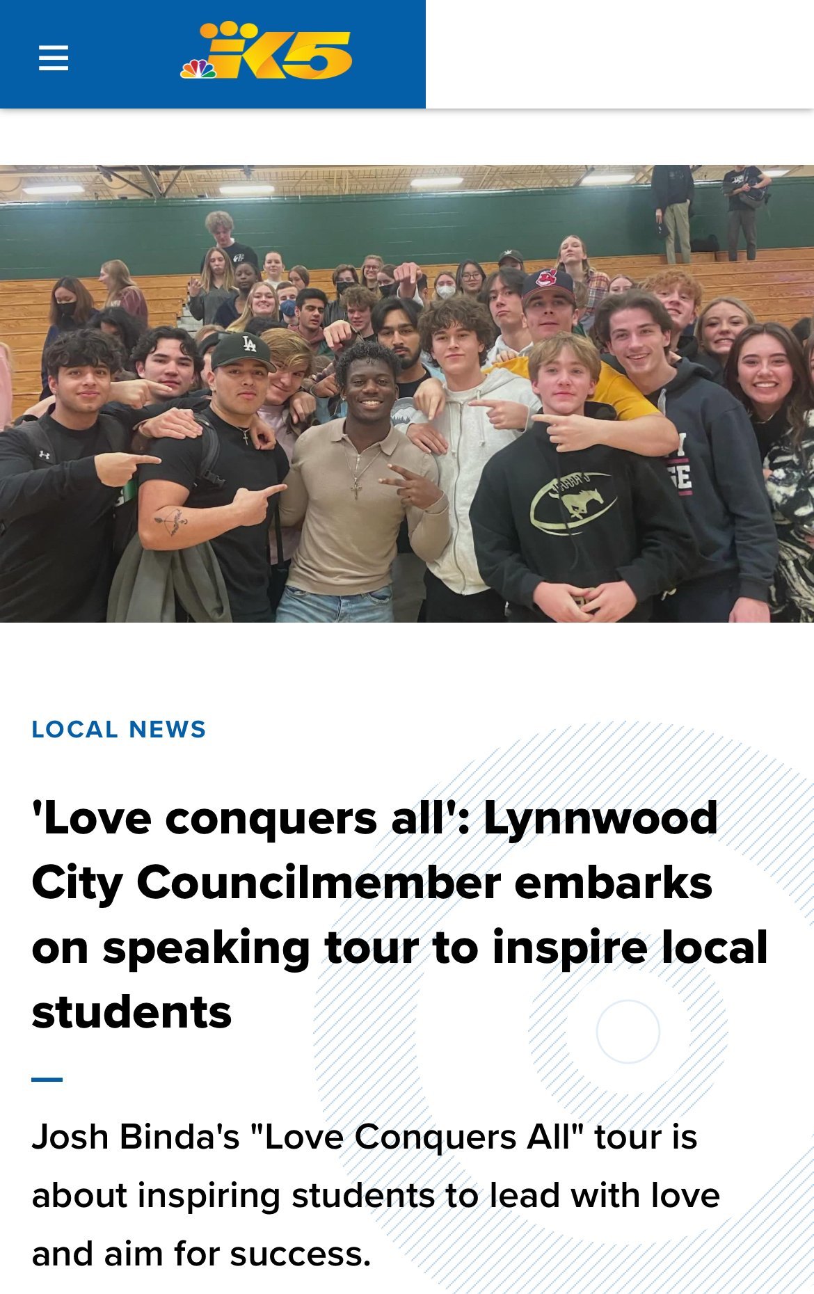 Group of students in a gymnasium posing with a speaker from a local news event, emphasizing student inspiration and leadership.
