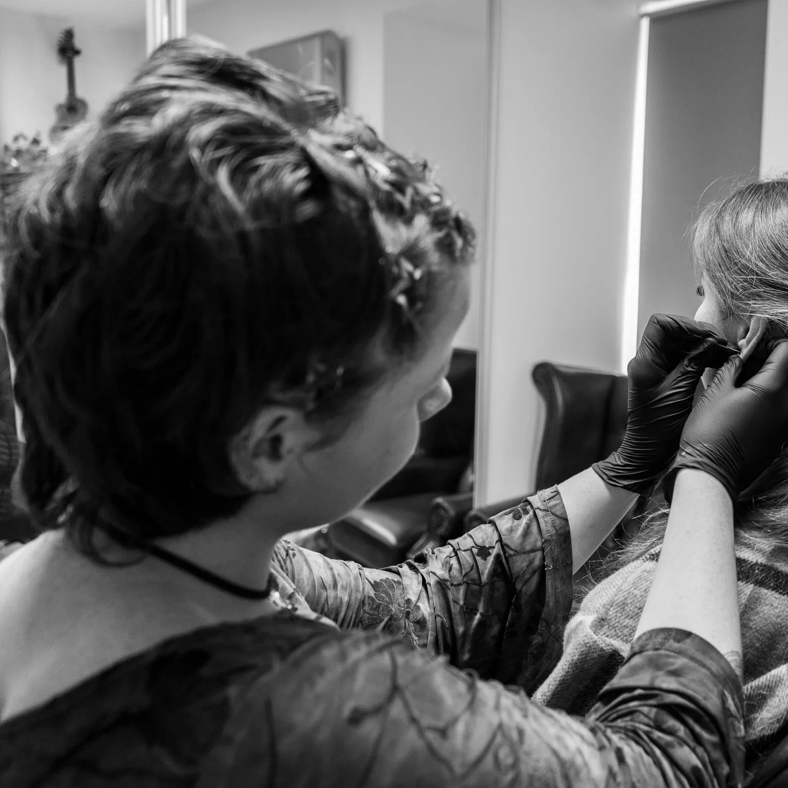 Tattoo artist in black gloves tattooing a woman's ear.