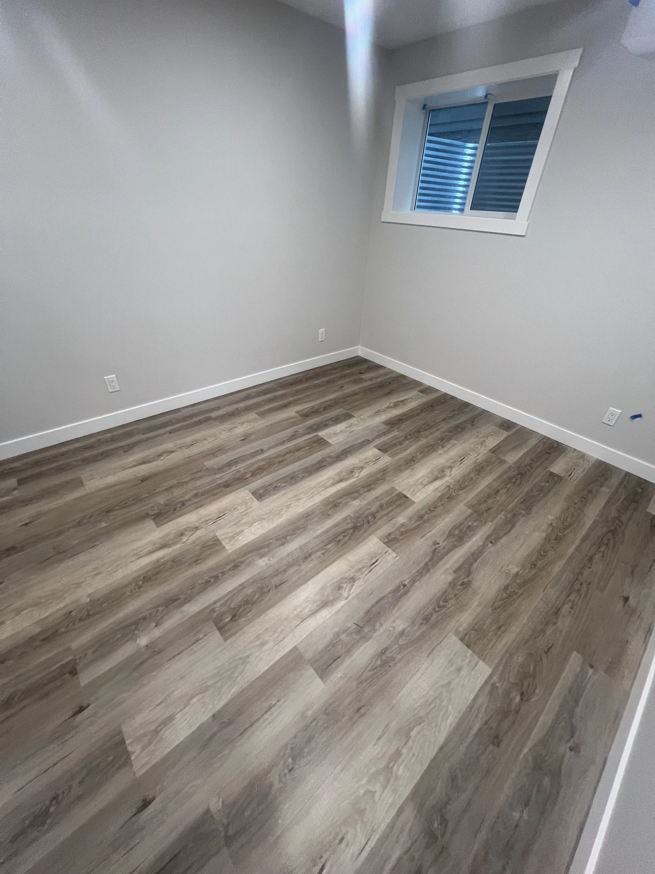 Empty room with wood laminate flooring, beige walls, and a window with white trim.