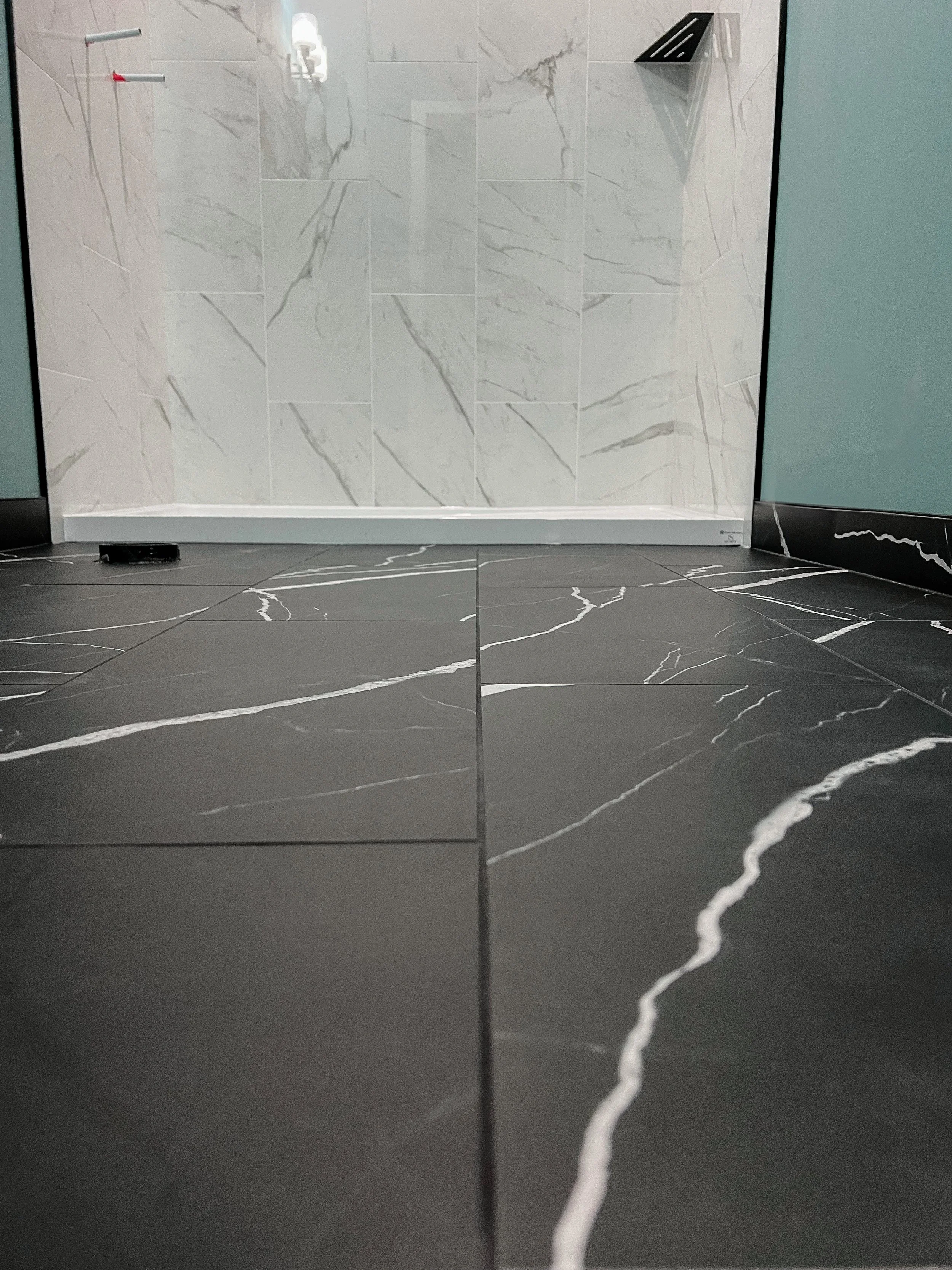Bathroom with large black floor tiles and white marble wall tiles, featuring a glass shower enclosure and a black corner shelf.