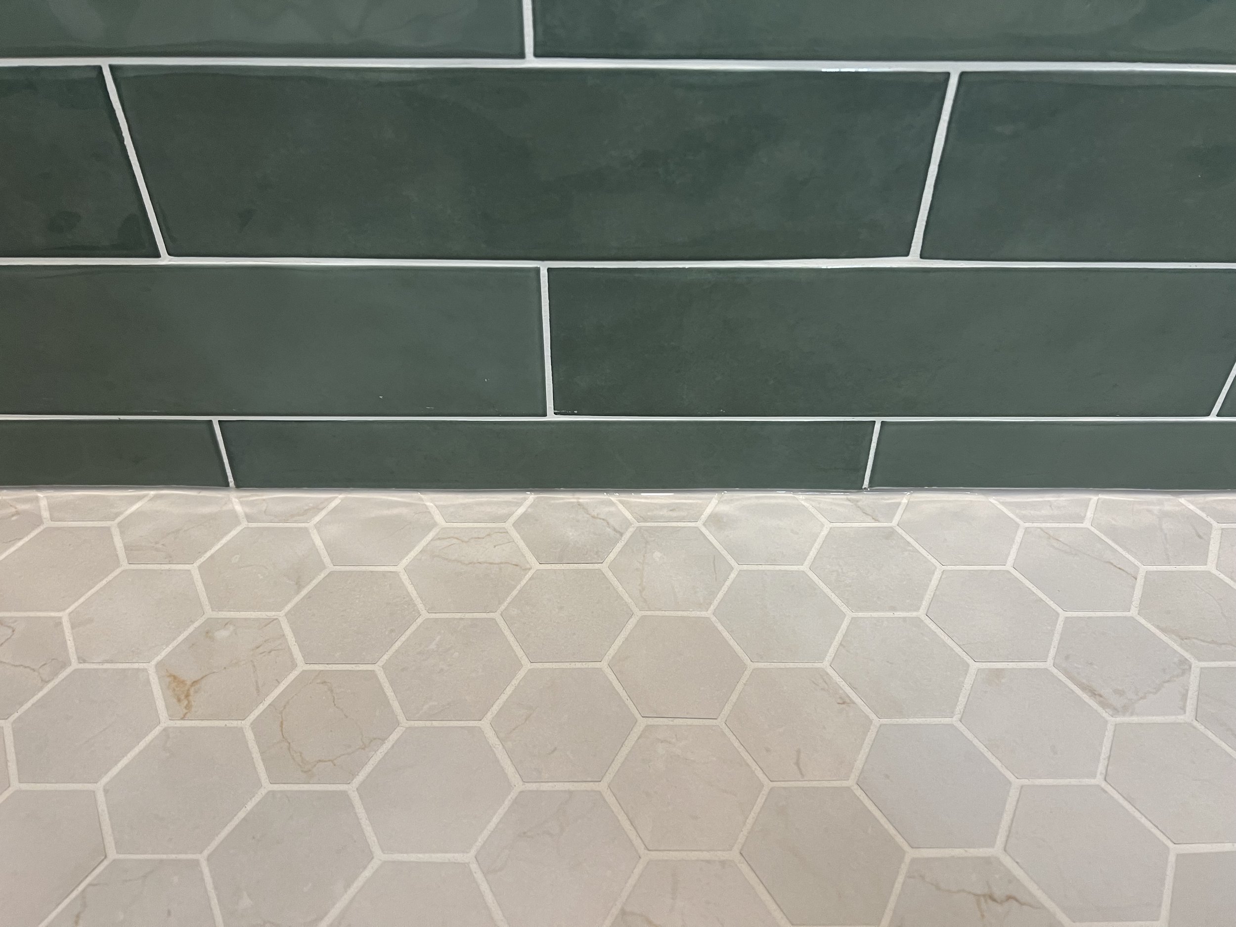 Green rectangular tile wall with white hexagonal tile floor.