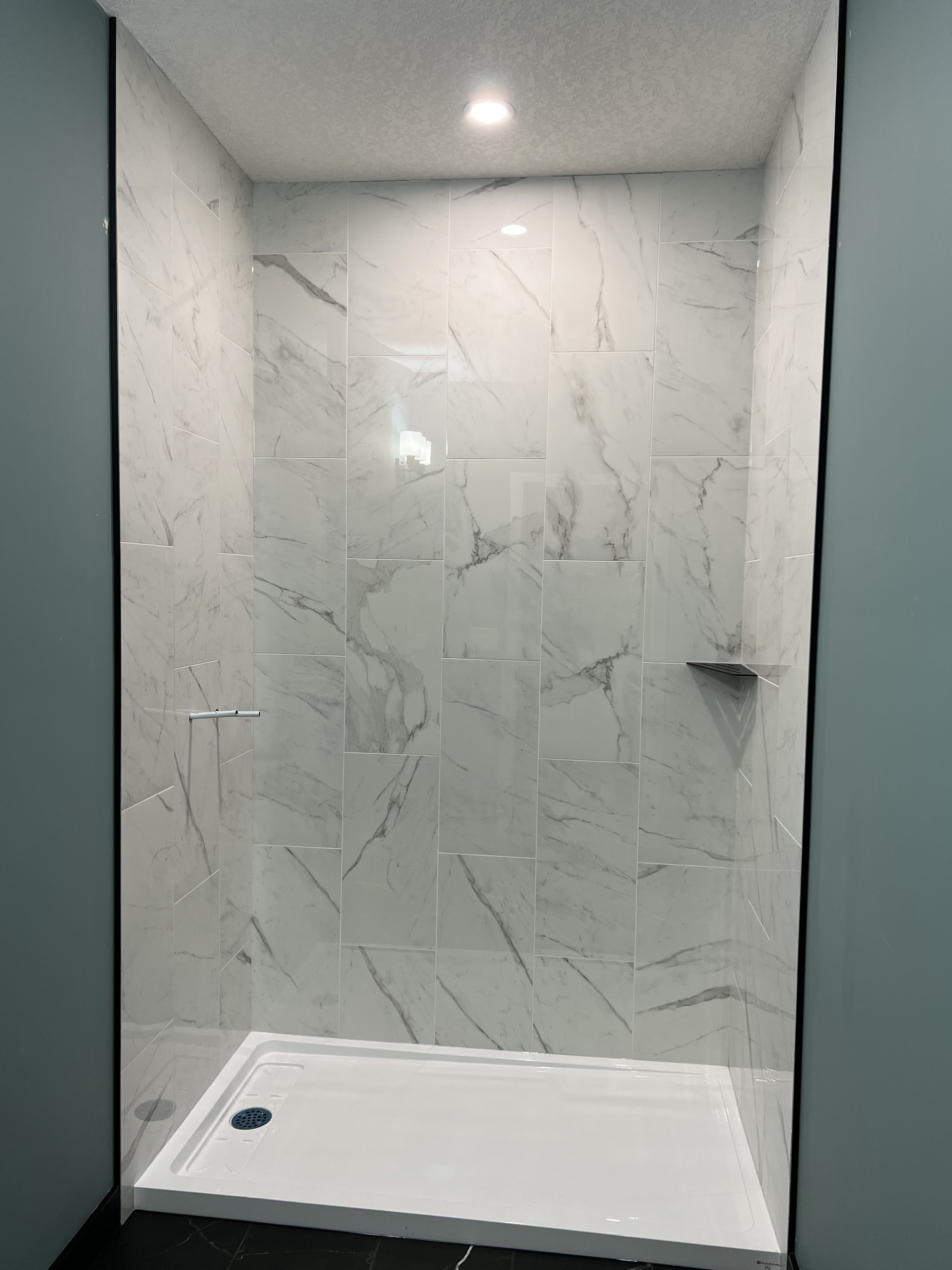 Modern shower stall with marble-patterned tiles and overhead lighting.