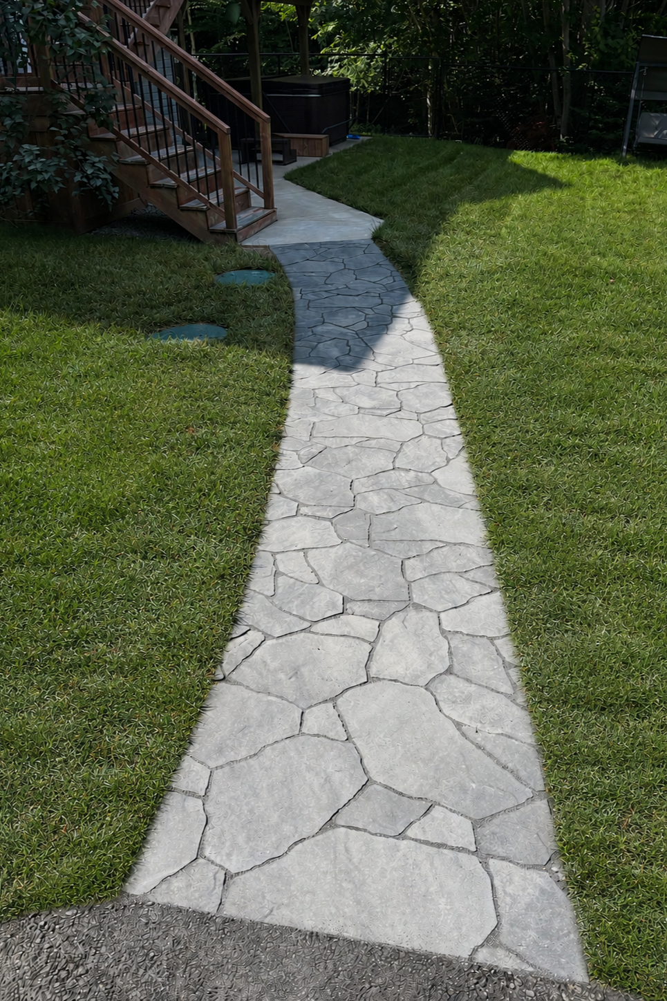 Concrete pathway leading to wooden deck with stairs and green lawn on both sides.