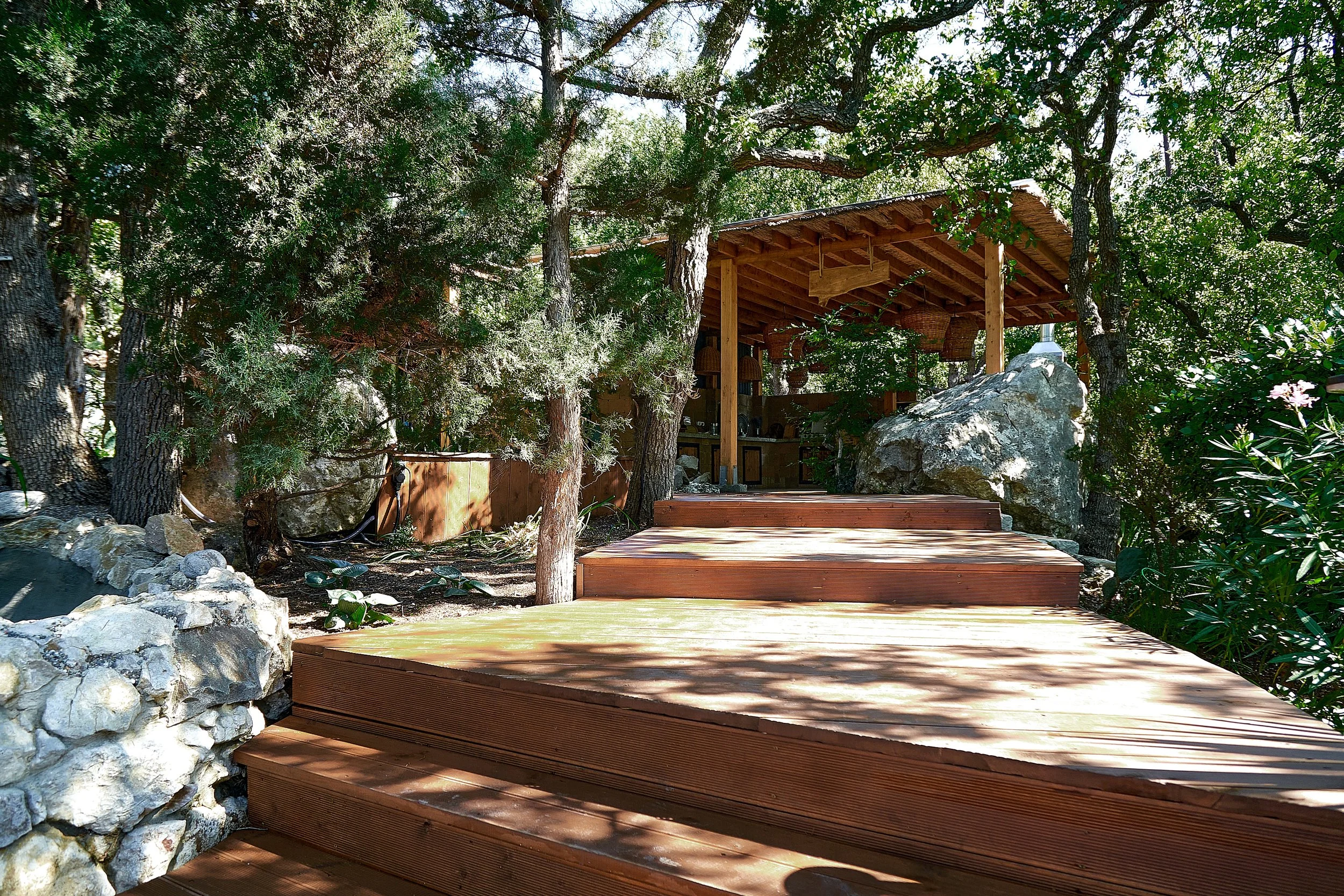 Wooden deck stairs leading to a shaded deck area surrounded by trees and rocks.