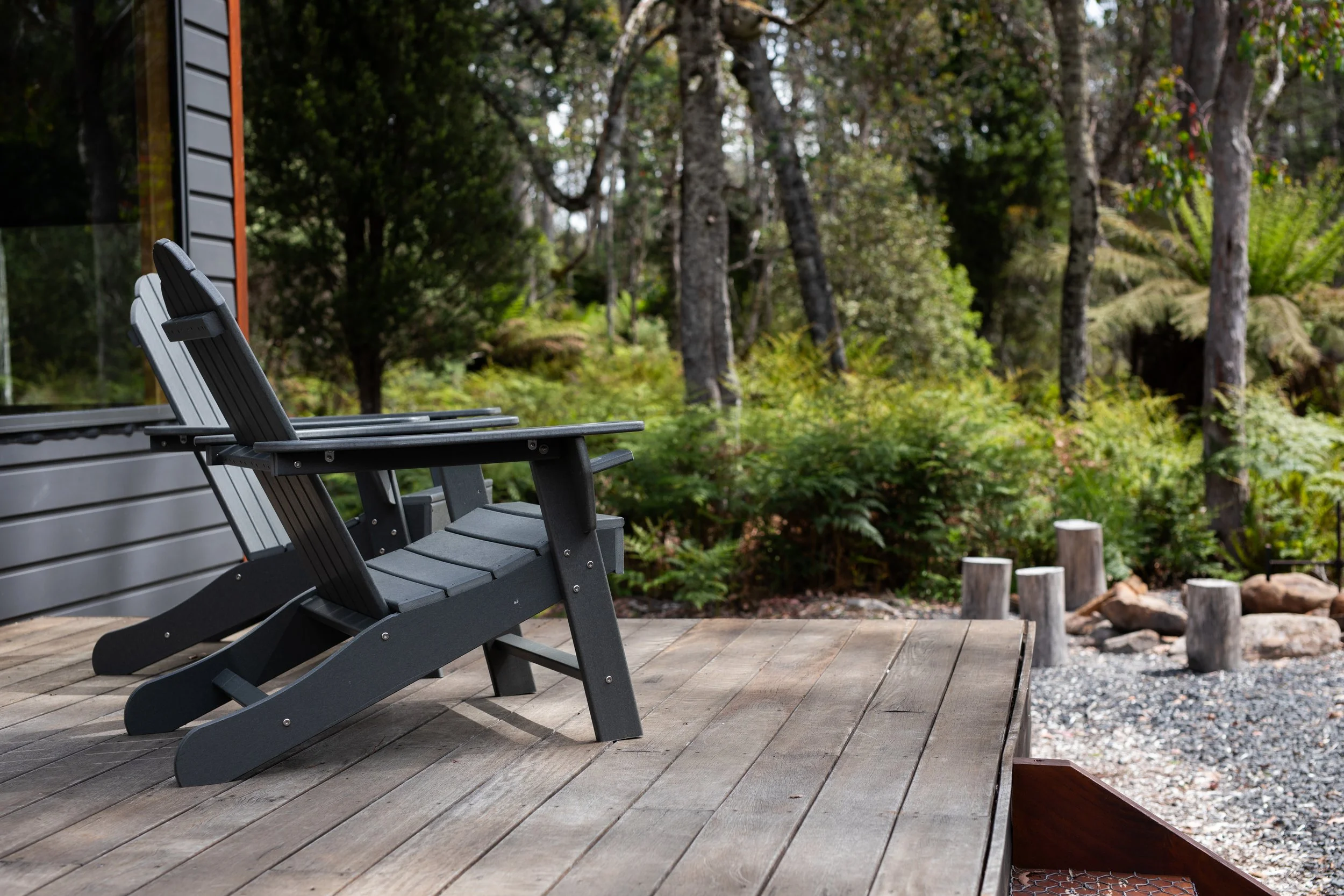 Black outdoor lounge chairs on a wooden patio facing an area of lush green trees and plants.