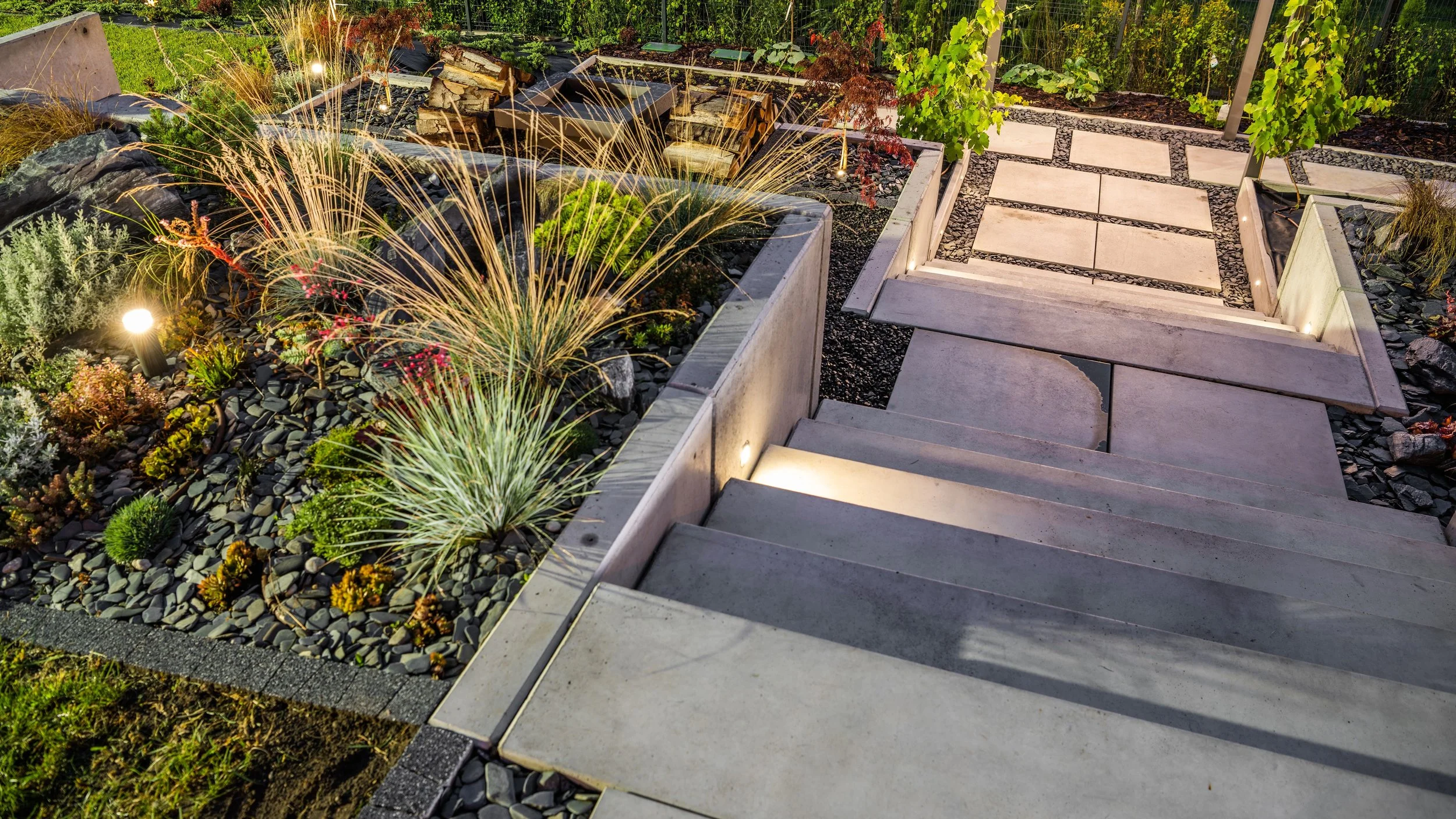 A modern outdoor garden with steps leading to a pathway, surrounded by landscaped plants and decorative gravel.