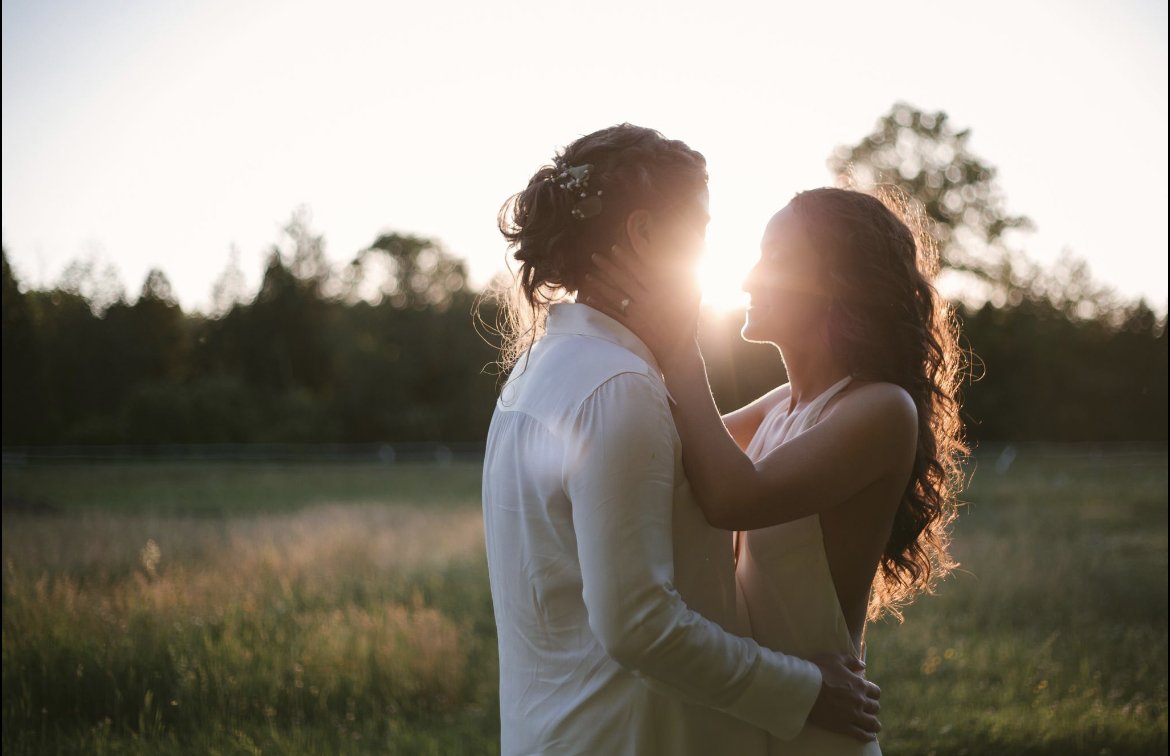 Two women embracing outdoors at sunset, holding each other's face and smiling, with trees in the background.