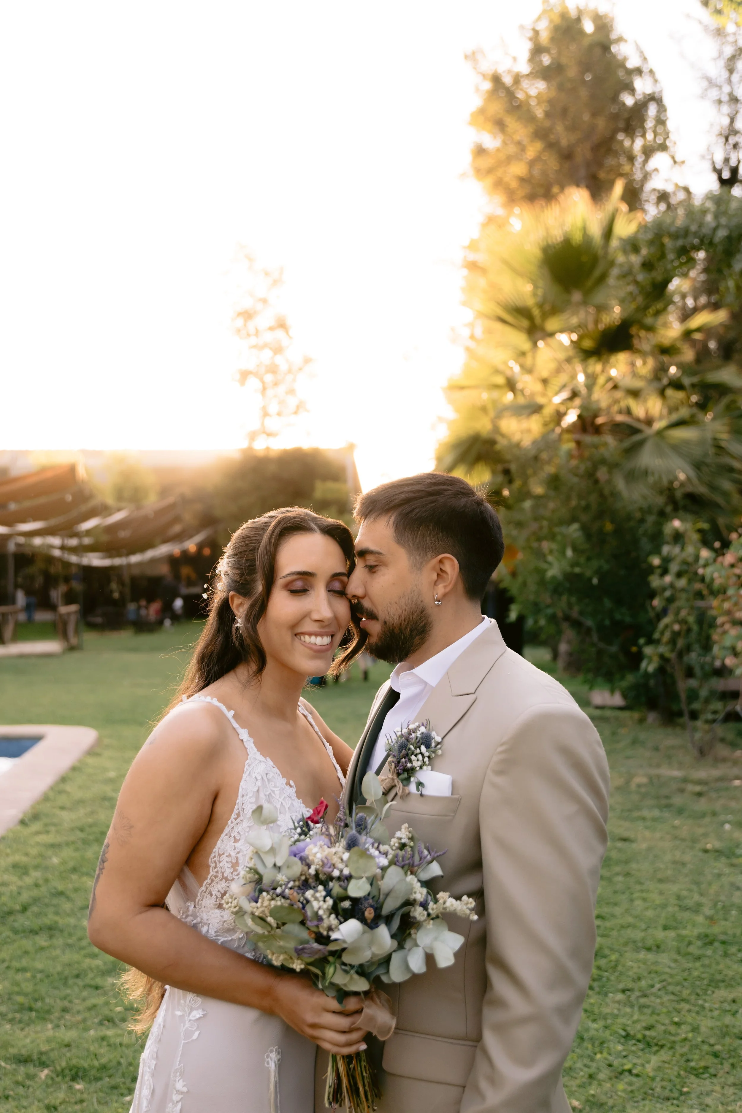 Novios abrazados al atardecer, con el sol filtrándose entre los árboles — Schulz Fotografía