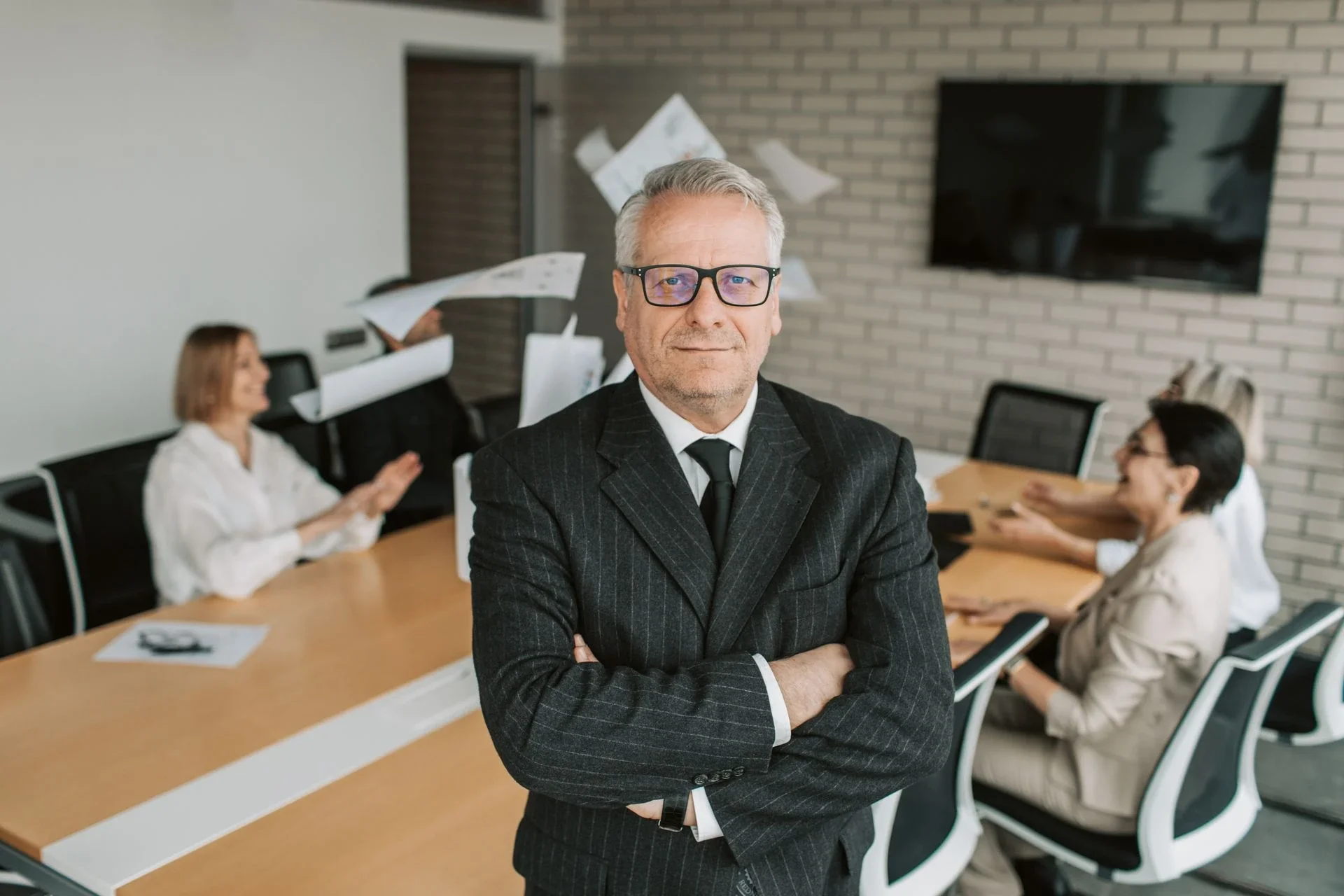 Business executive standing confidently in a meeting room with team engaged in discussion behind