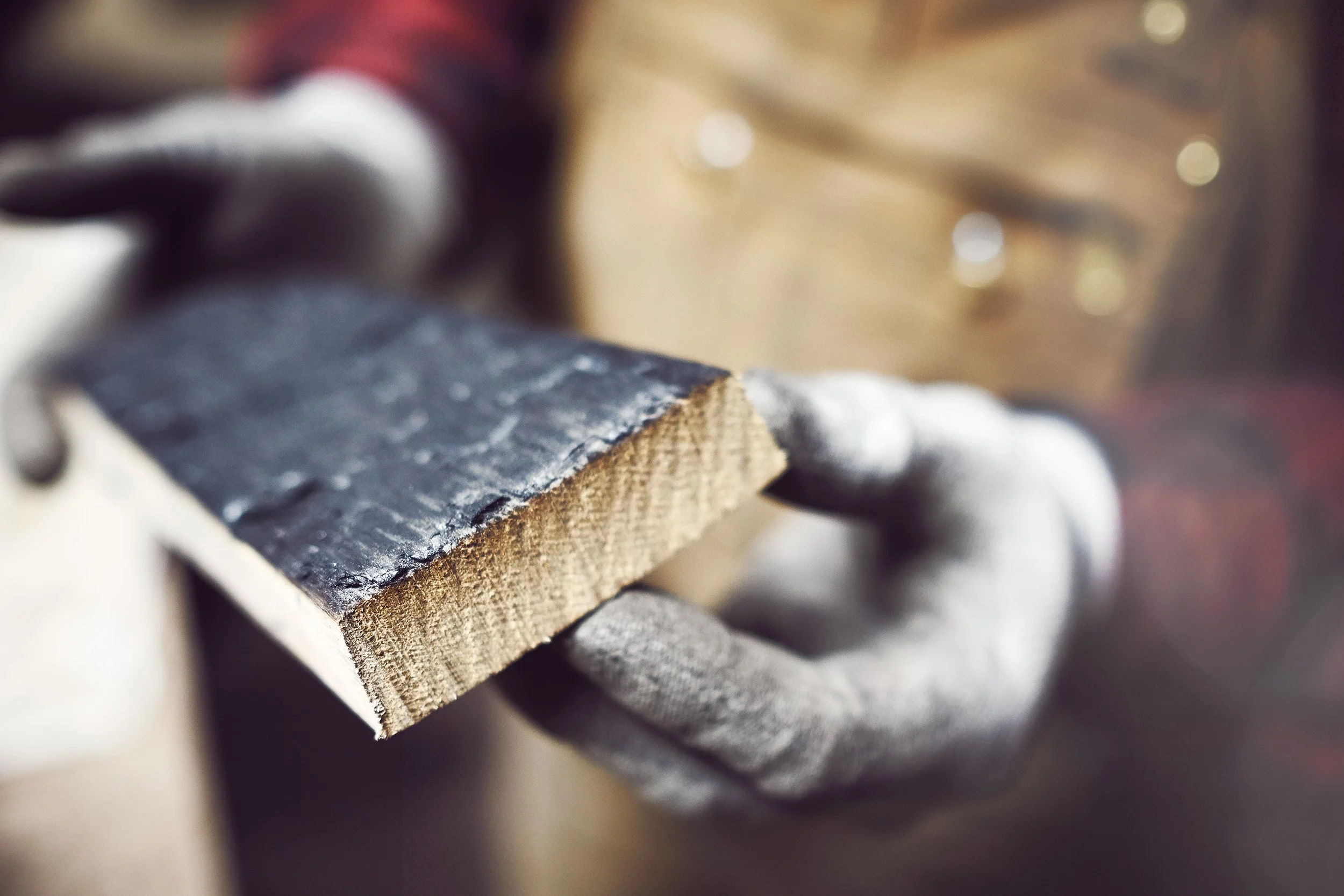 Gloved hands holding an oak stave charred black on one face