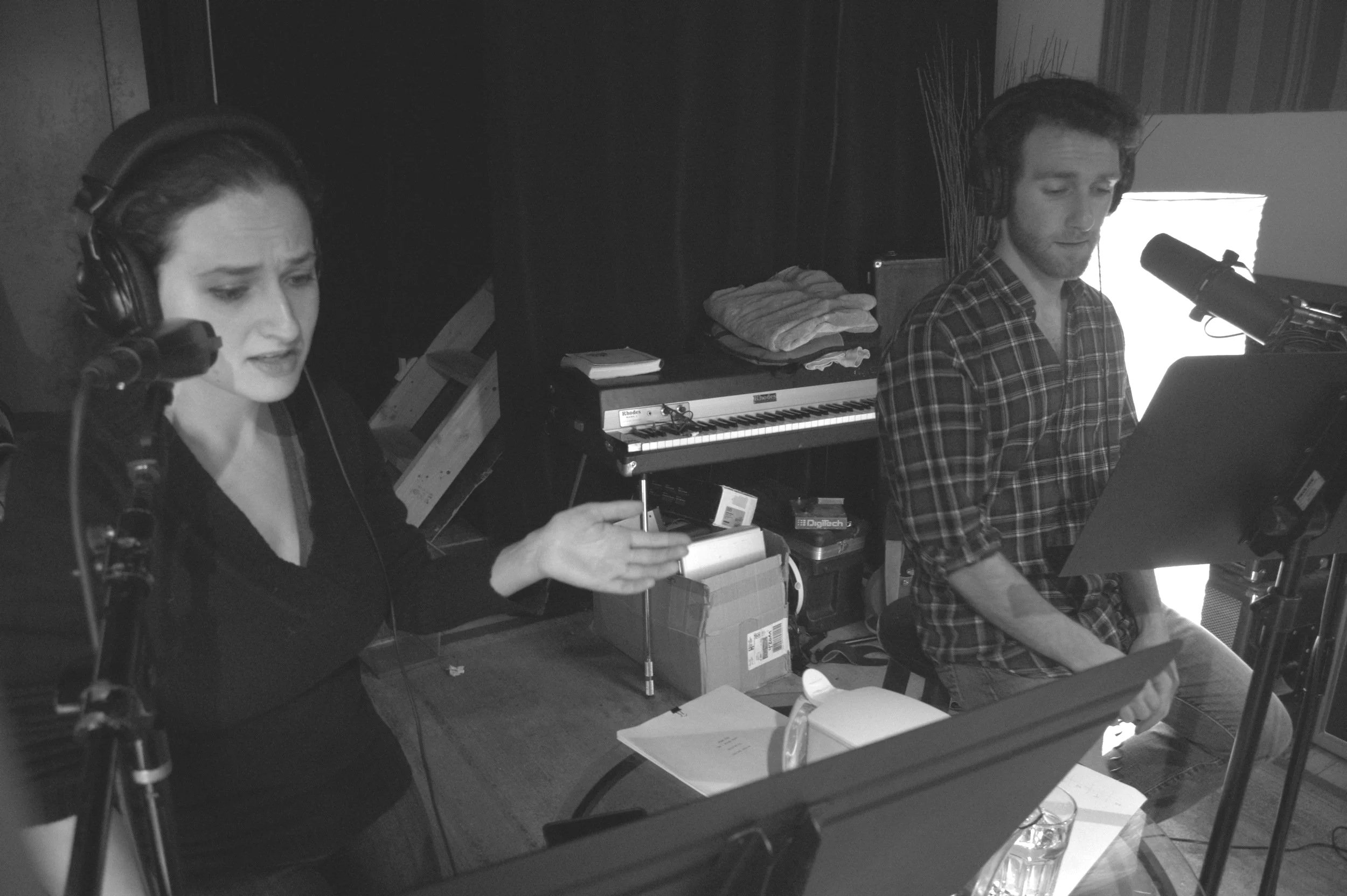 Two figures at microphones. A woman on the left gestures as she speaks.