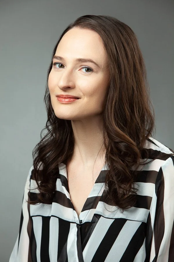 A headshot of a woman in a black and white striped shirt smiling slightly