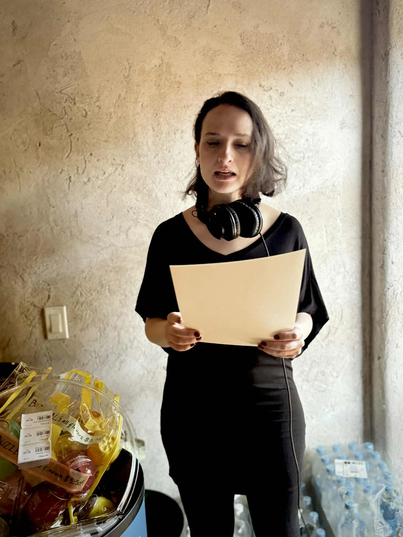 A woman in black with headphones around her neck looks down at a piece of paper