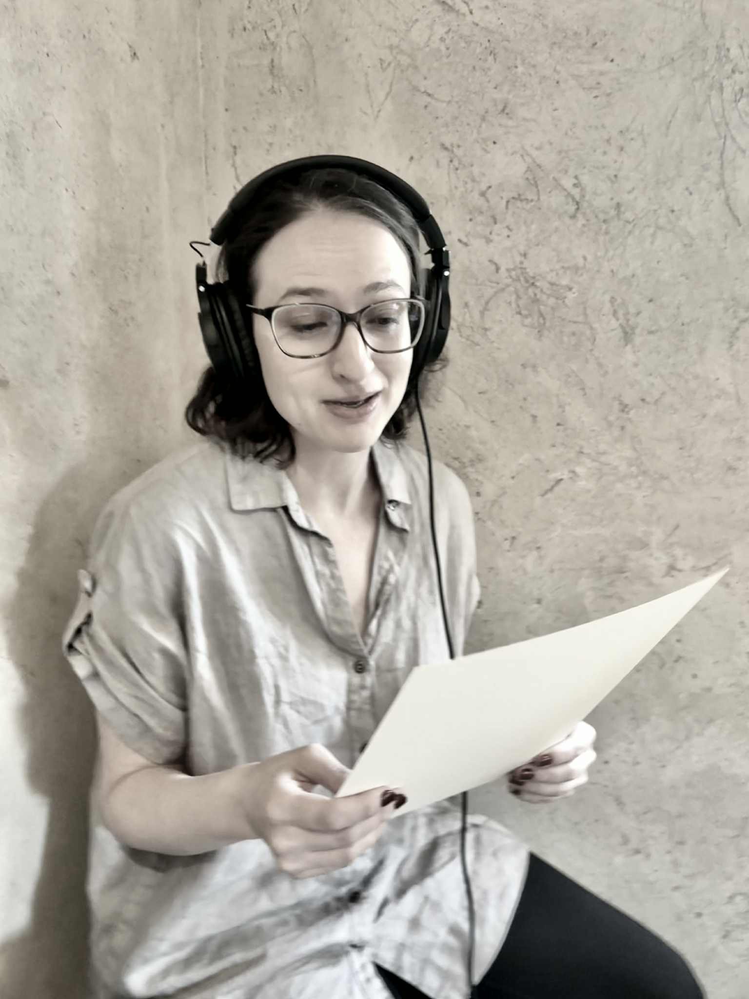 A woman wearing headphones sits and looks at a piece of paper
