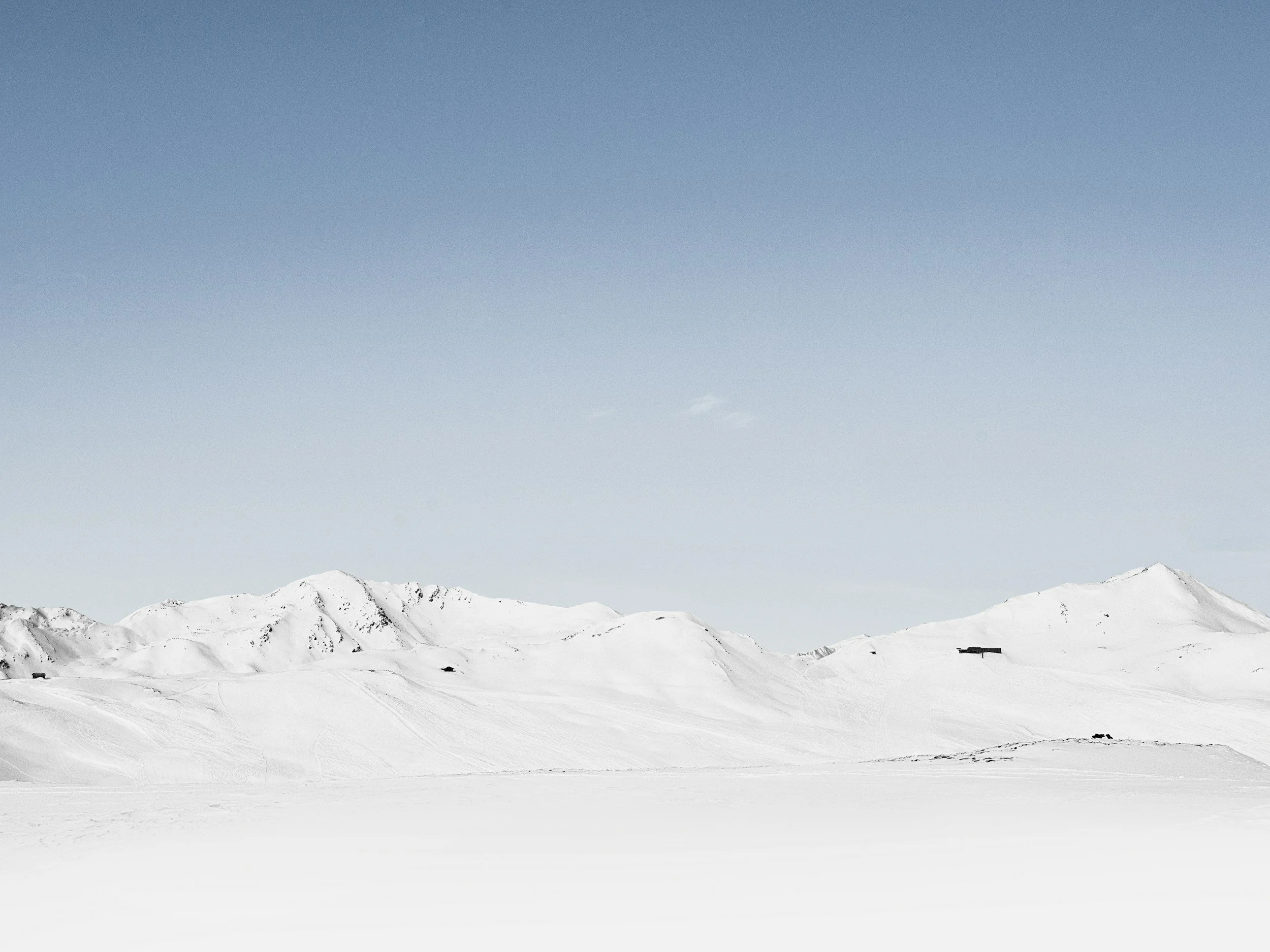 Snowy mountain landscape with clear blue sky and a few small clouds, a small building or structure at the base of the mountains, from Jimmy Swinder.