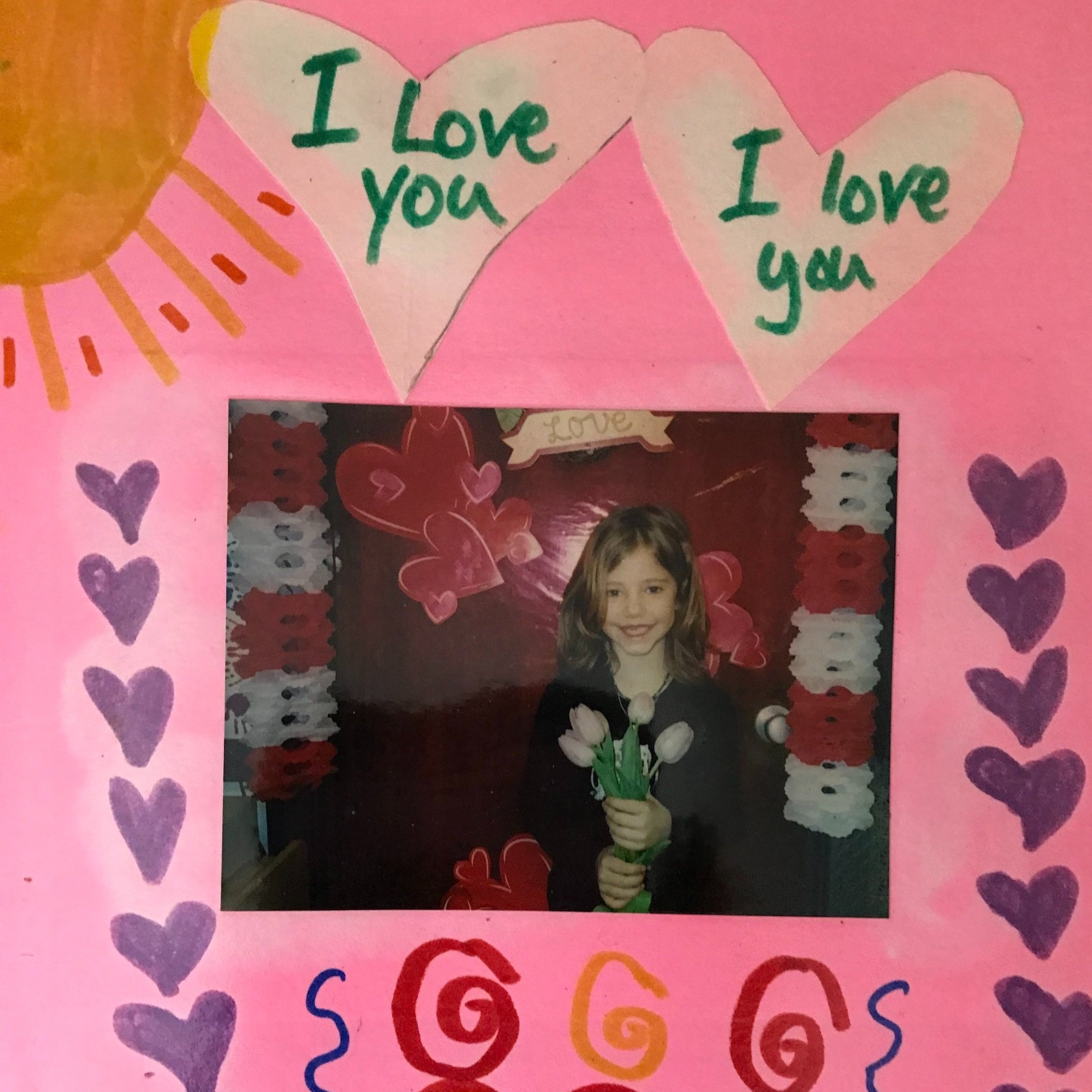 Handmade Valentine card with a photo of a child holding flowers, surrounded by heart and sun decorations, with "I Love You" written in hearts.