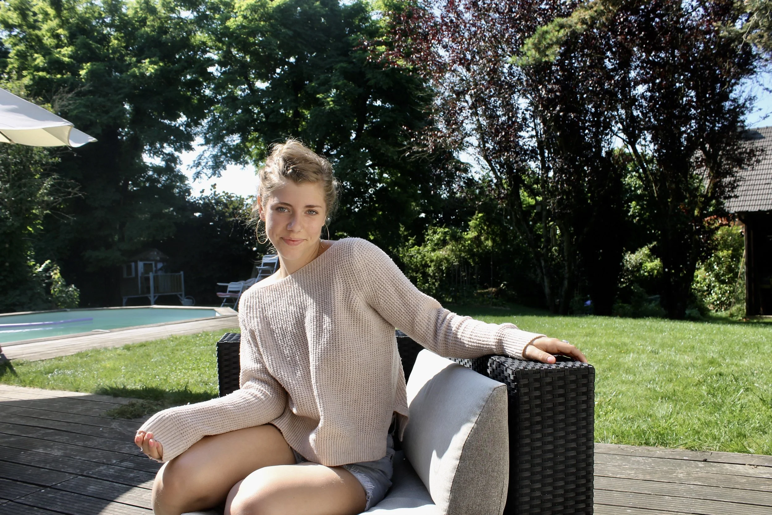 Louisa sitting on outdoor sofa near a pool in her French father's garden