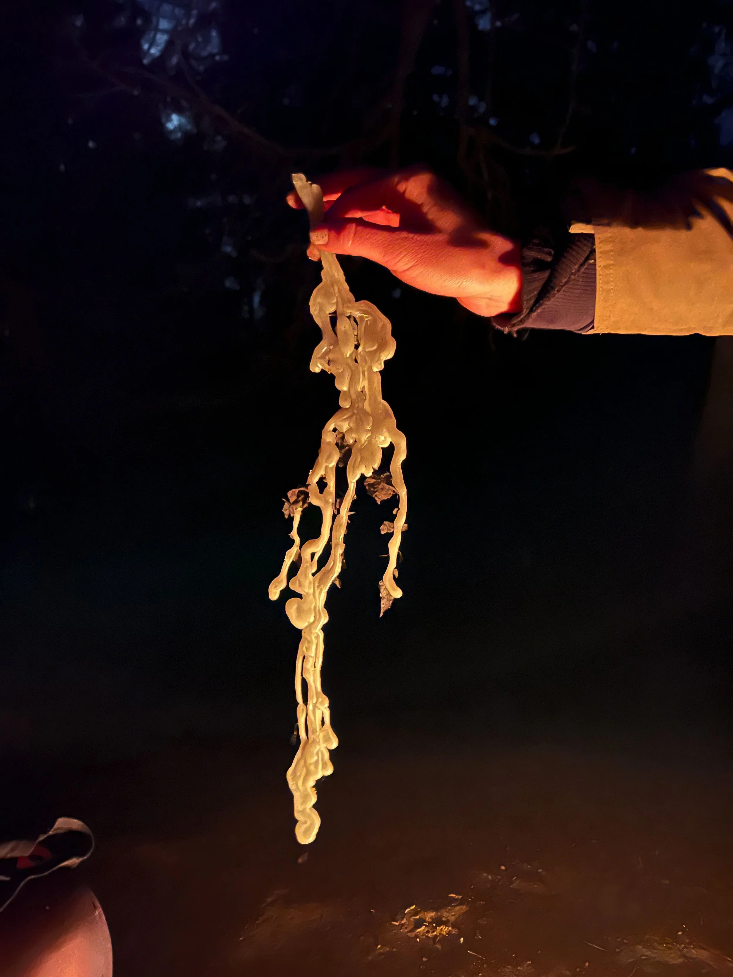 Person holding a melted, stringy, white candle outdoors at night.