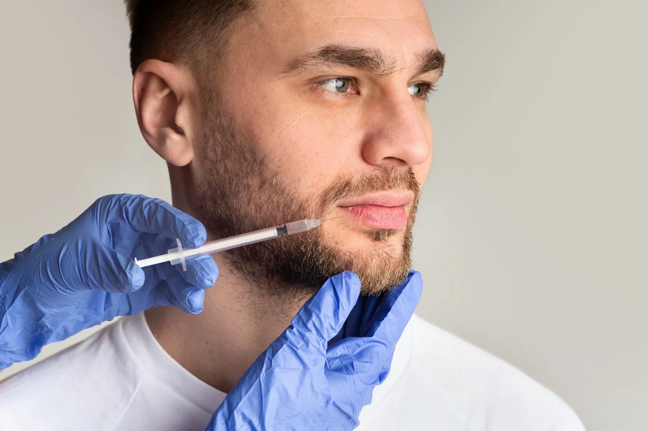 A man having a medical injection administered in his face by a healthcare professional wearing blue gloves.