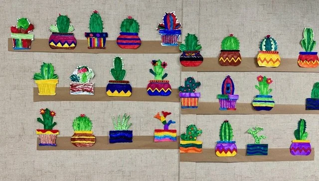 Colorful paper cacti and succulent artwork displayed on wooden shelves.