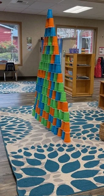 A tall, cone-shaped tower made of colorful plastic cups stacked in a playroom or classroom.